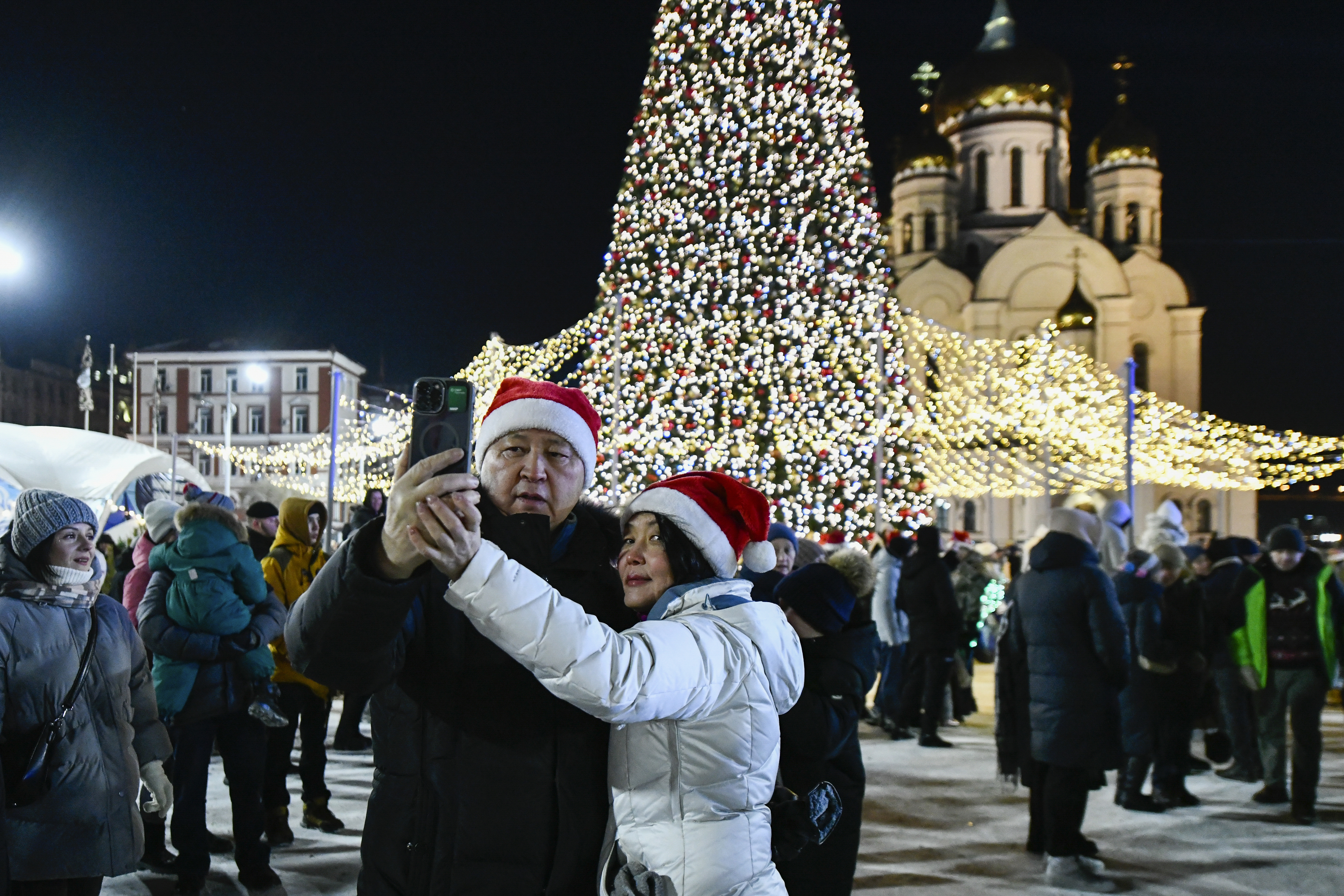 A couple make a selfie as other people gather in the center of the Russian far east port of Vladivostok, Russia, Tuesday, Dec. 31