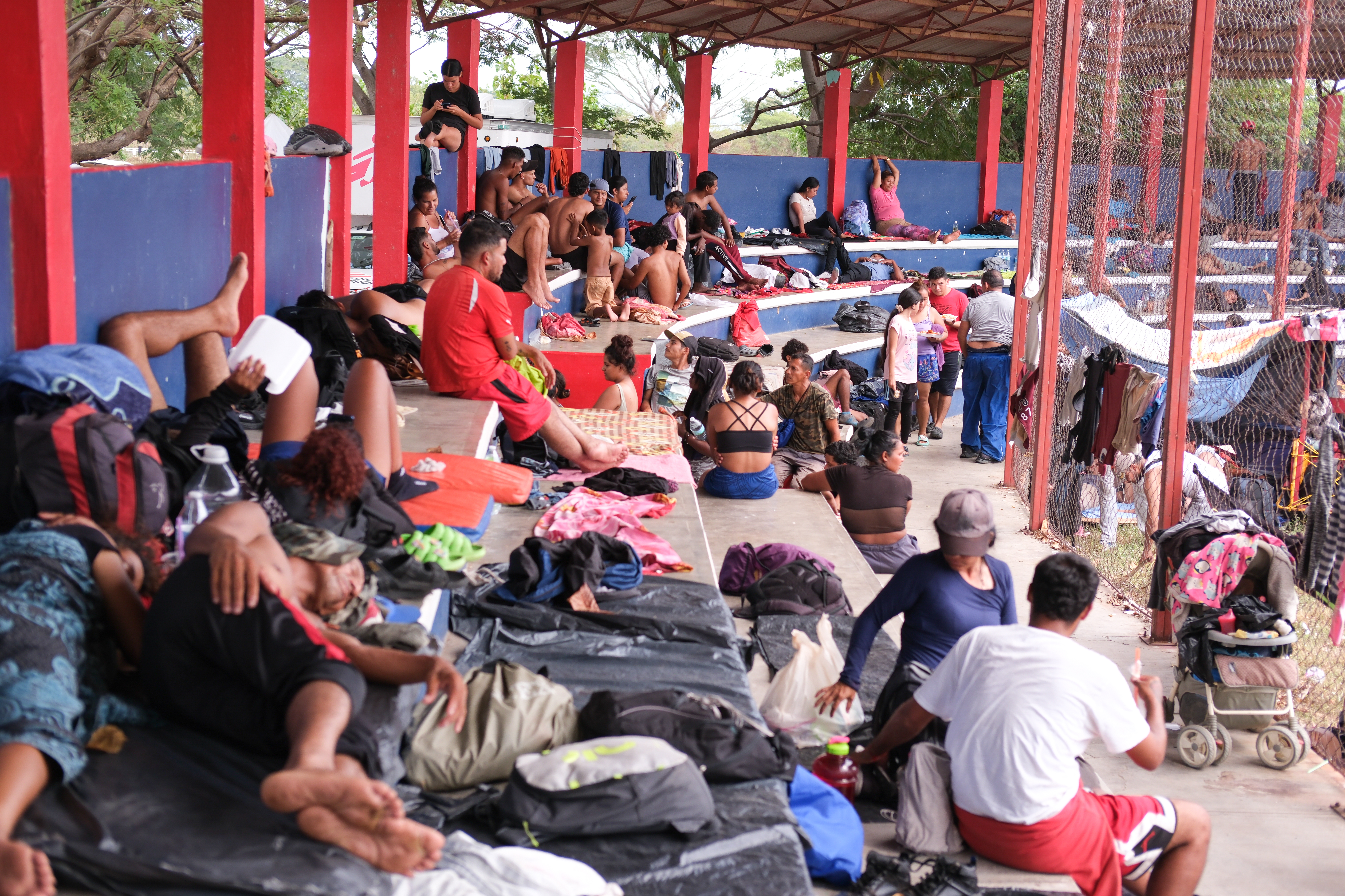 Migrants and asylum seekers gather on tiered seating under an awning in Santiago Niltepec, Mexico