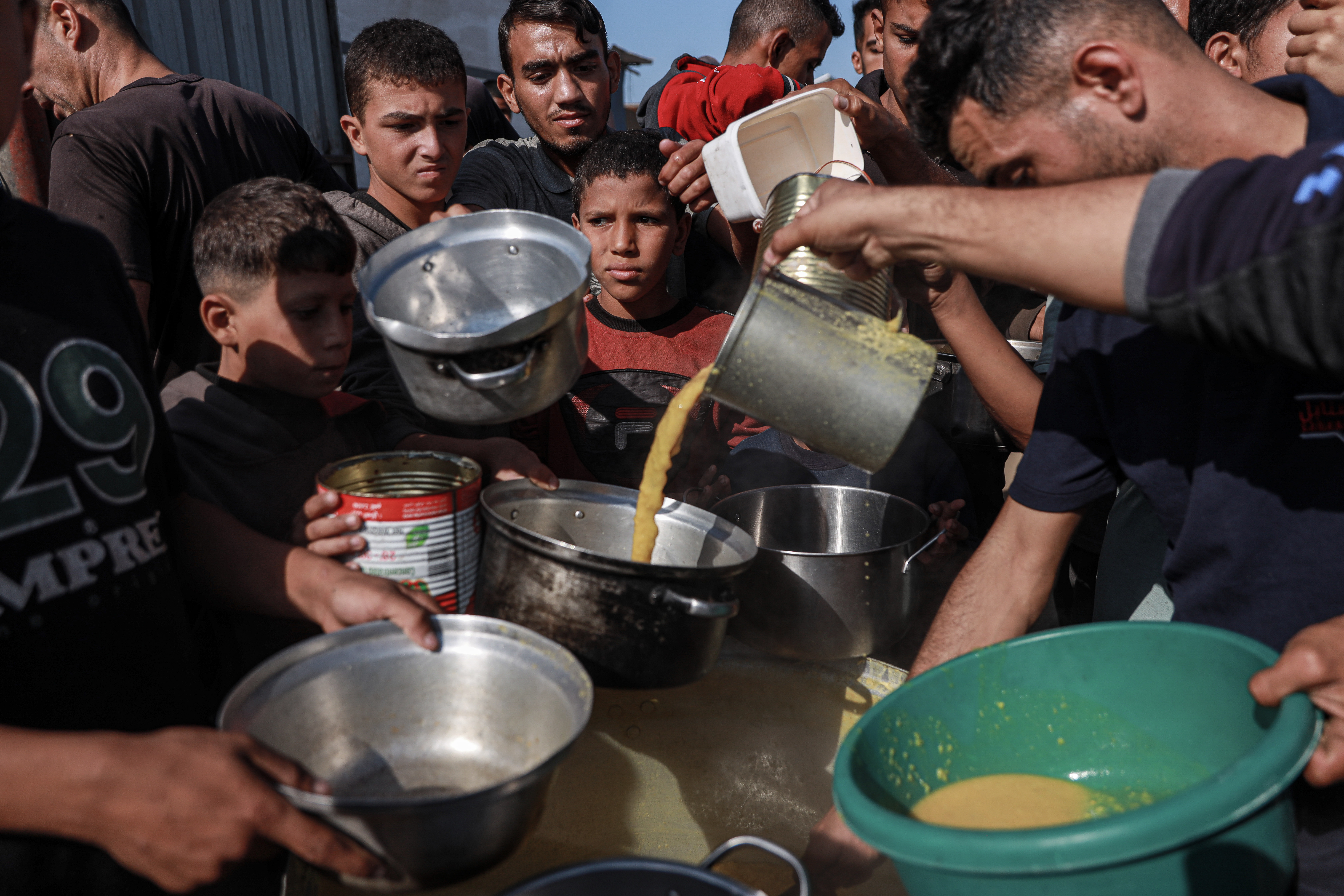 A group of displaced people gather at Sanabel's Tekkiyyat in Mawasi, Khan Younis, in Gaza’s south, which provides daily meals [Abdelhakim Abu Raish/Al Jazeera]