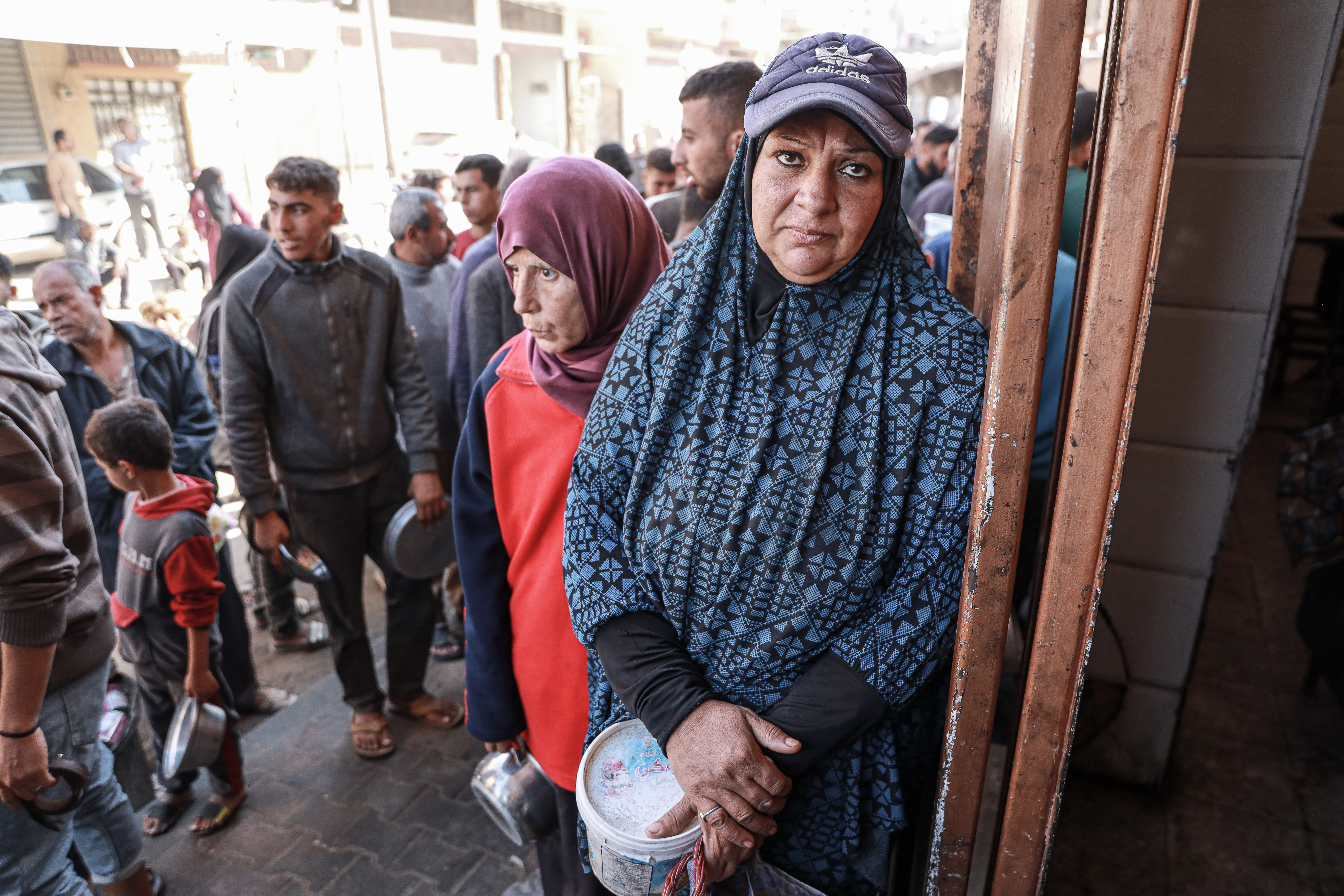 Ghada al-Kafarna waits at a community kitchen in Deir al-Balah to receive a meal of lentils for her children [Abdelhakim Abu Raish/Al Jazeera]