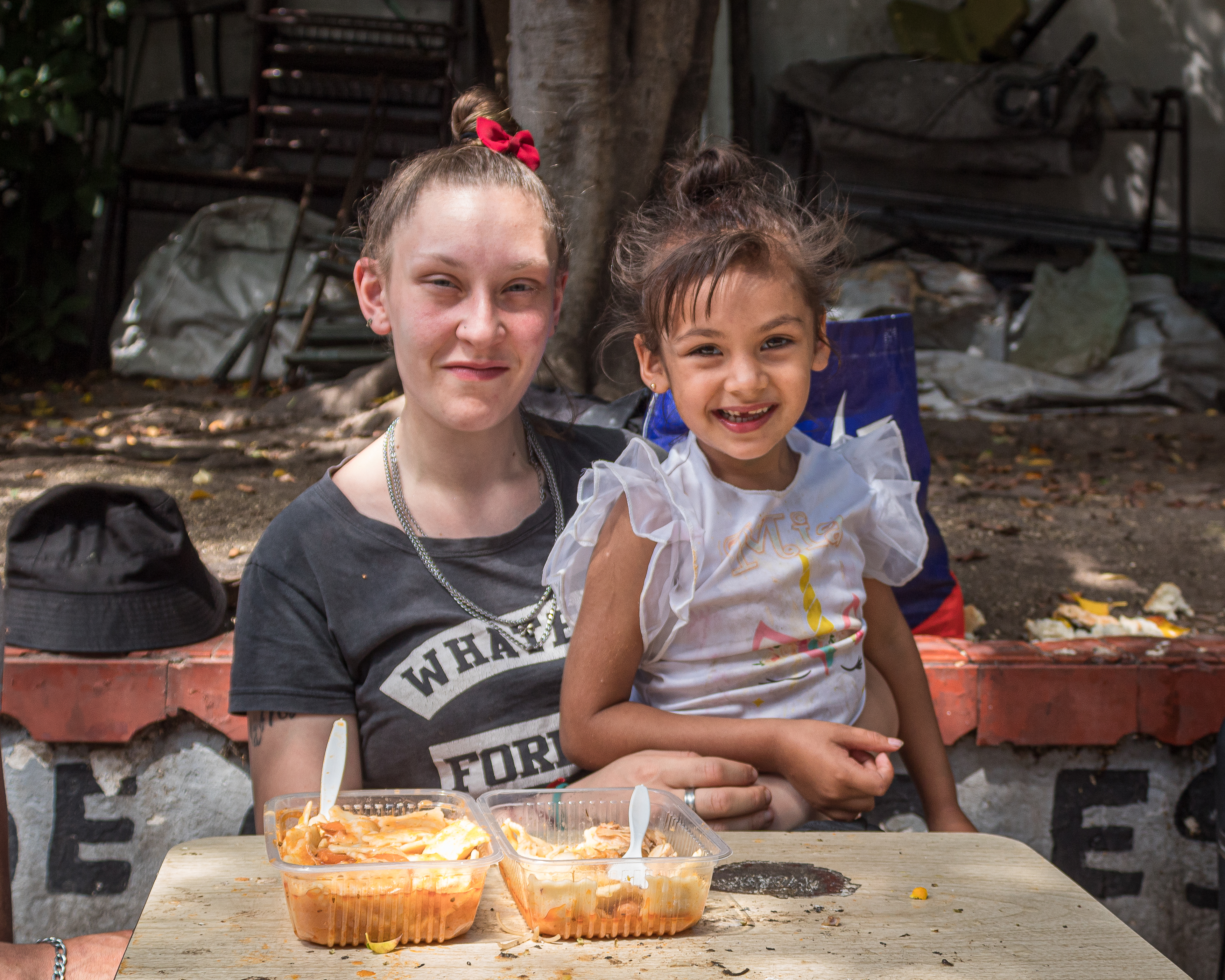 Marianela Abasto and her daughter sit in front of two trays of ravioli at an outdoor table.