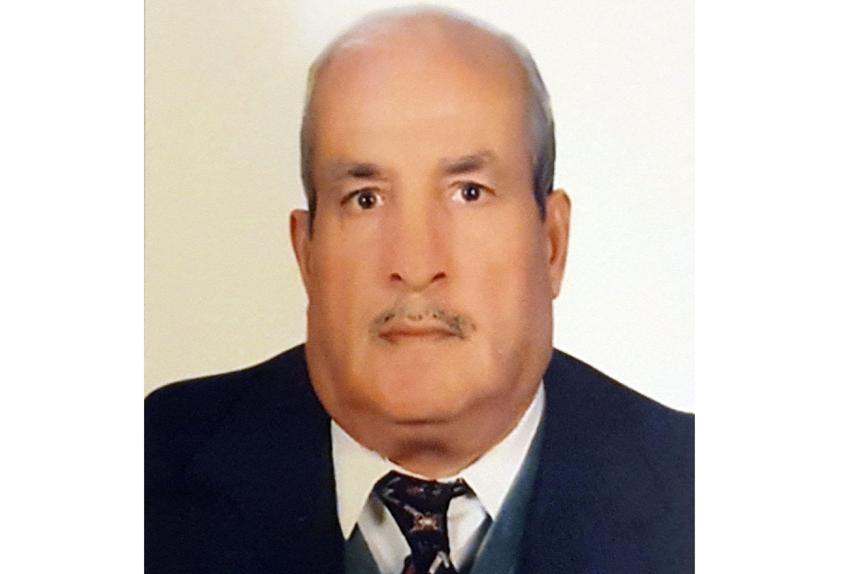A passport photo of a man with a mustache in a black suit