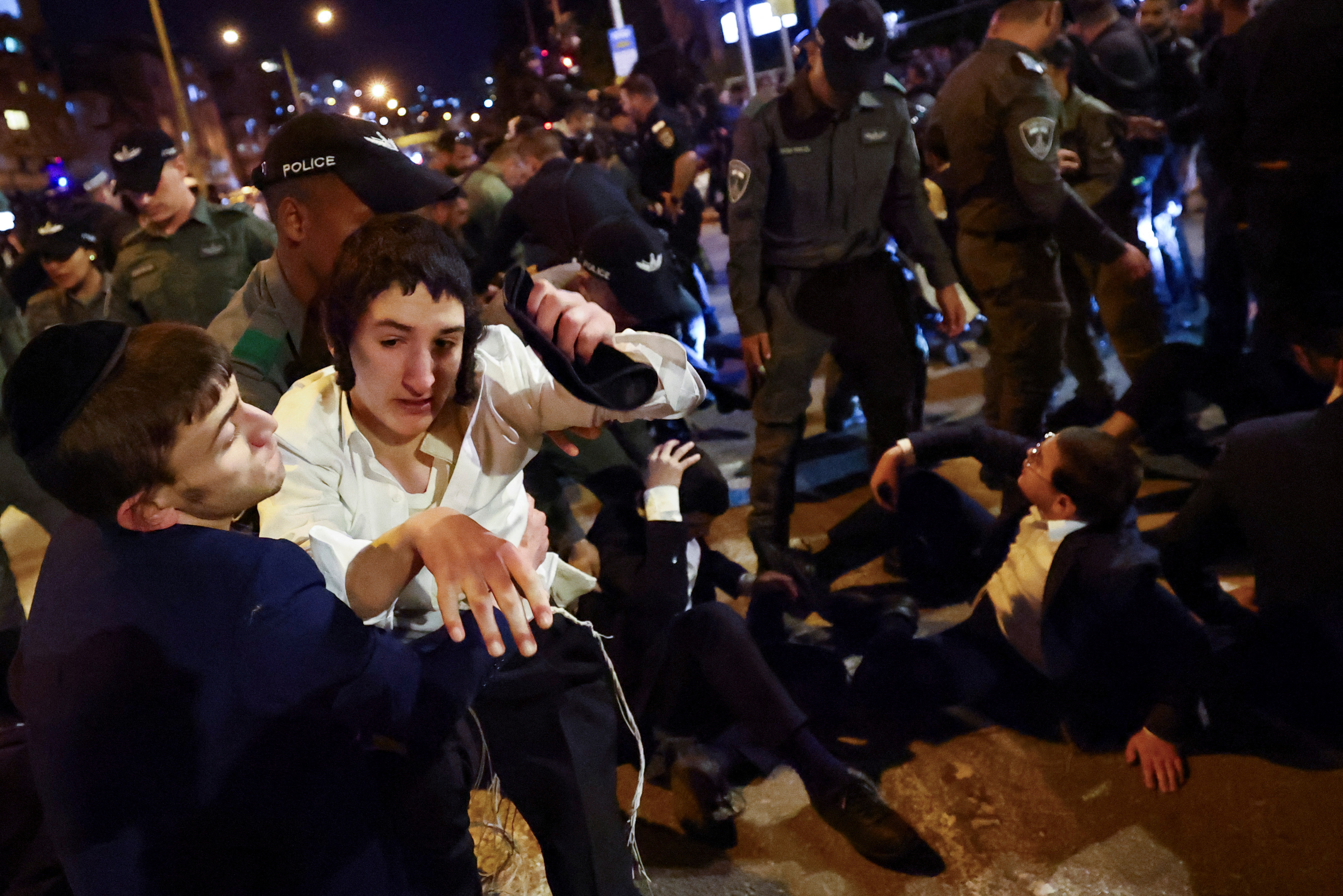 Police officers detain a demonstrator as Ultra-Orthodox Jewish men block a road in protest against attempts to recruit men from their community to Israel's military, on the outskirts of Bnei Brak, Israel, December 24, 2024. REUTERS/Kai Pfaffenbach