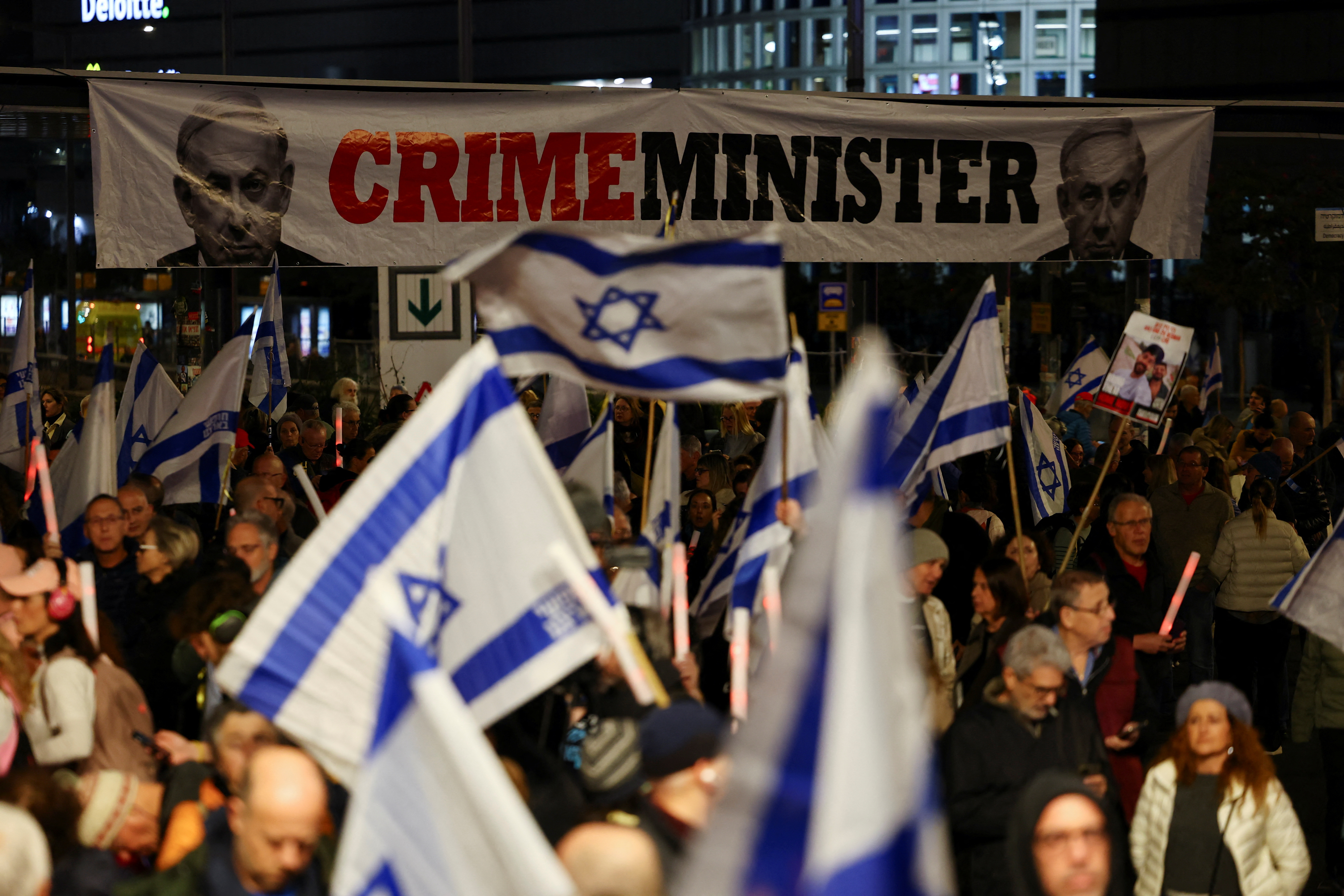 Crowd waves Israeli flags in front of a banner that depicts Israeli Prime Minister Benjamin Netanyahu and the words ' Crime Minister'