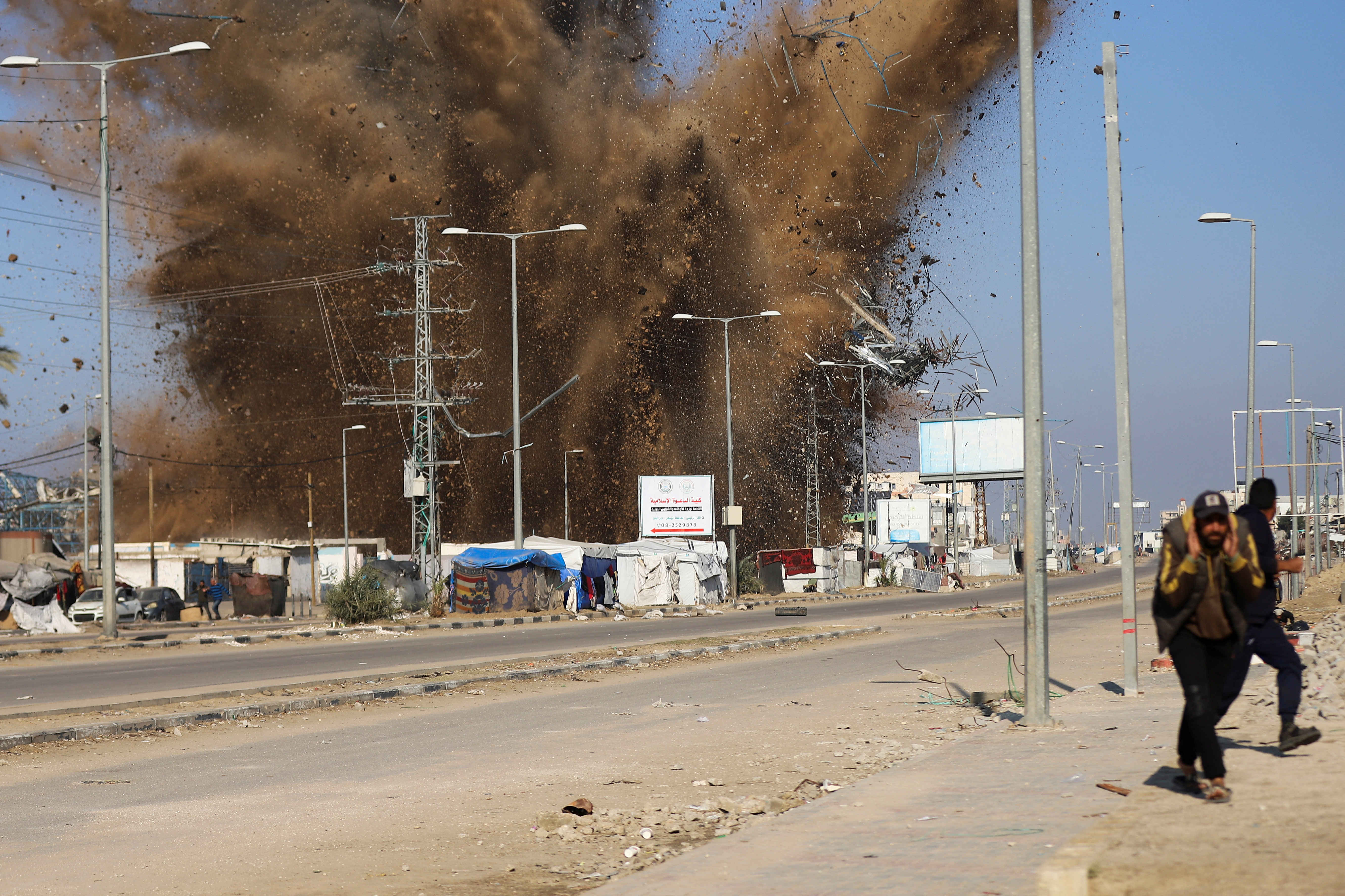 Palestinians take cover as sand and debris scatter following an Israeli strike, amid the Israel-Hamas conflict, in Deir Al-Balah in the central Gaza Strip January 3