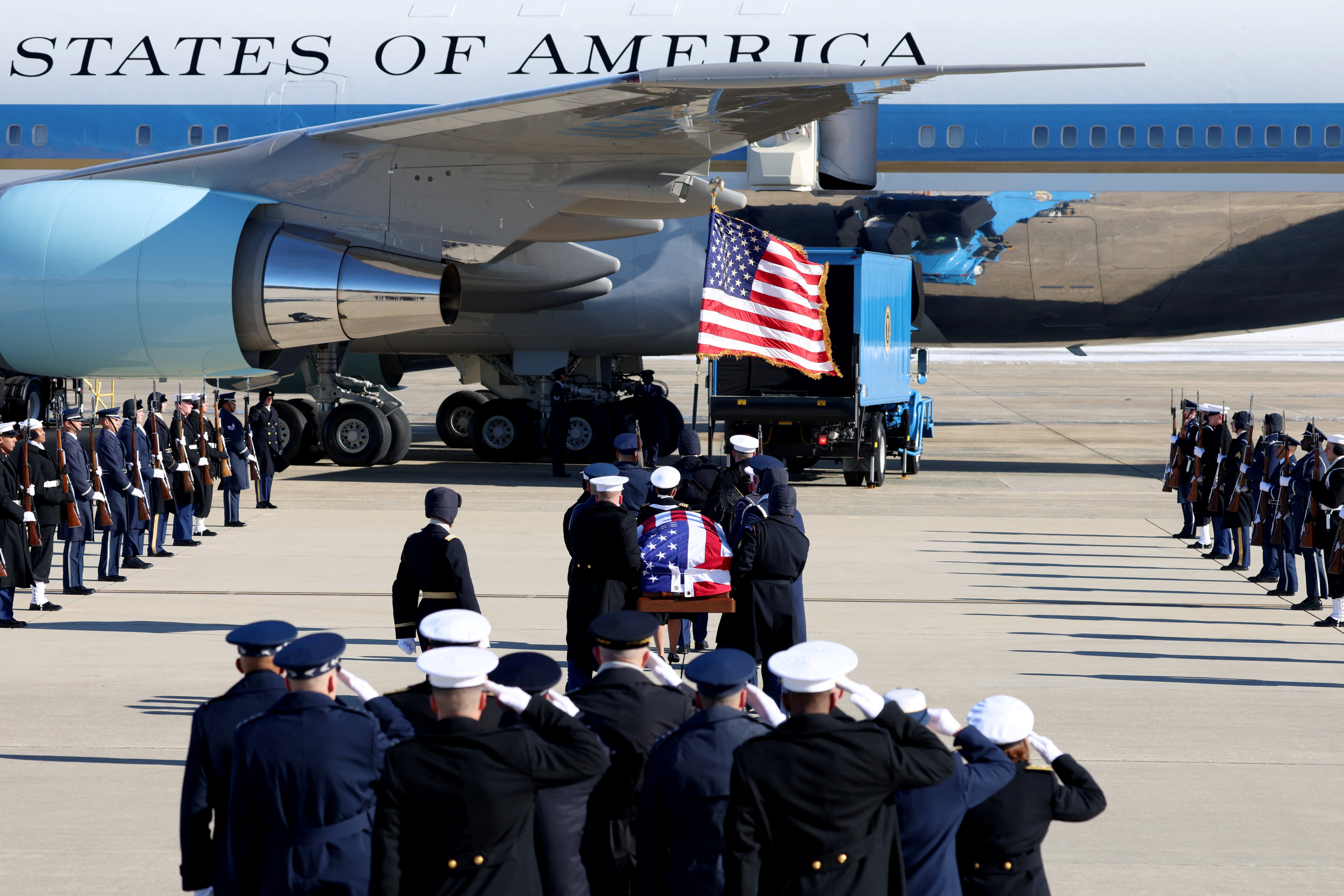 Service members carry the flag-draped coffin of Jimmy Carter to Special Air Mission, a US government plane.