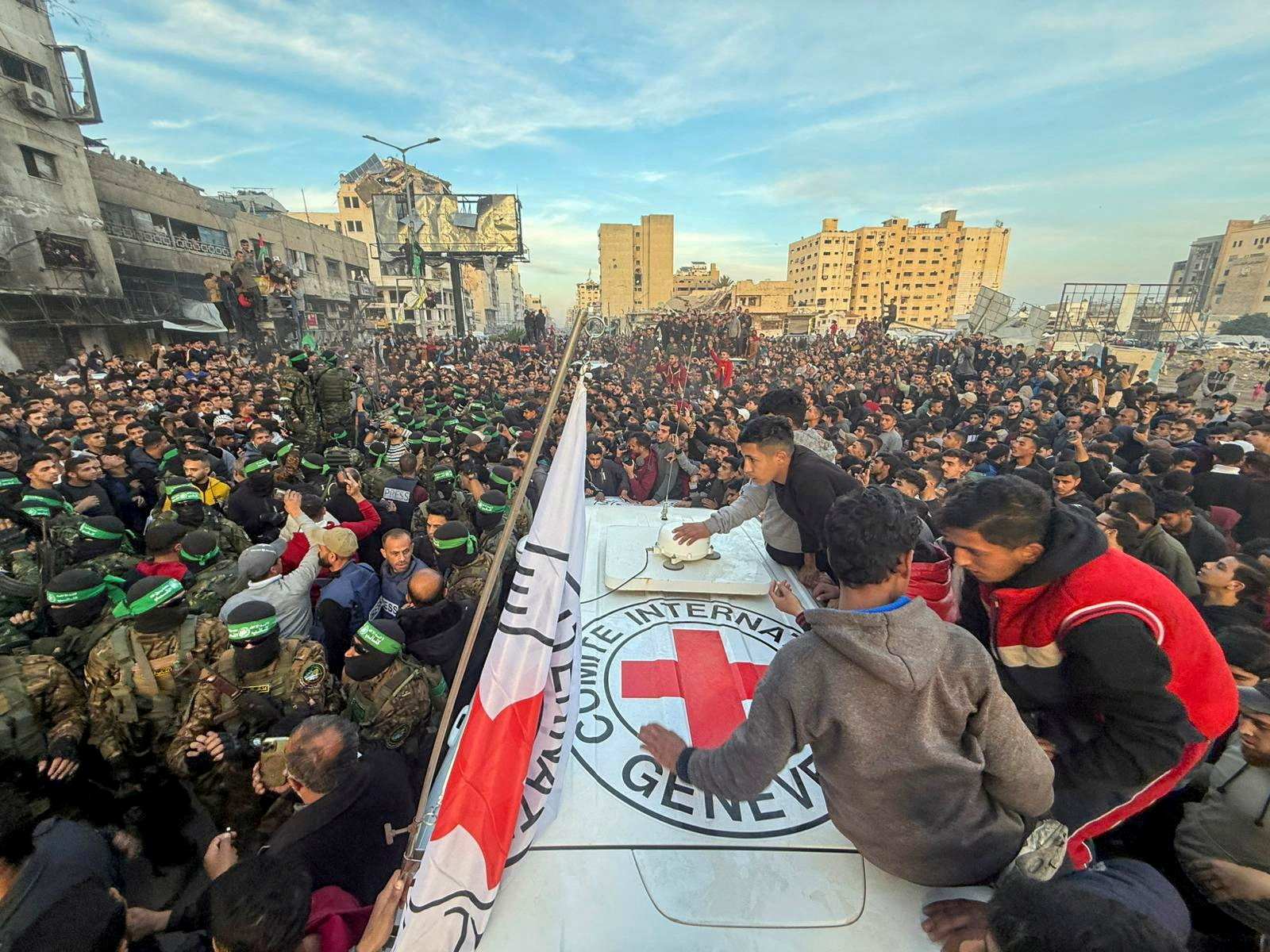 Hamas fighters and other Palestinians gather around a Red Cross vehicle.