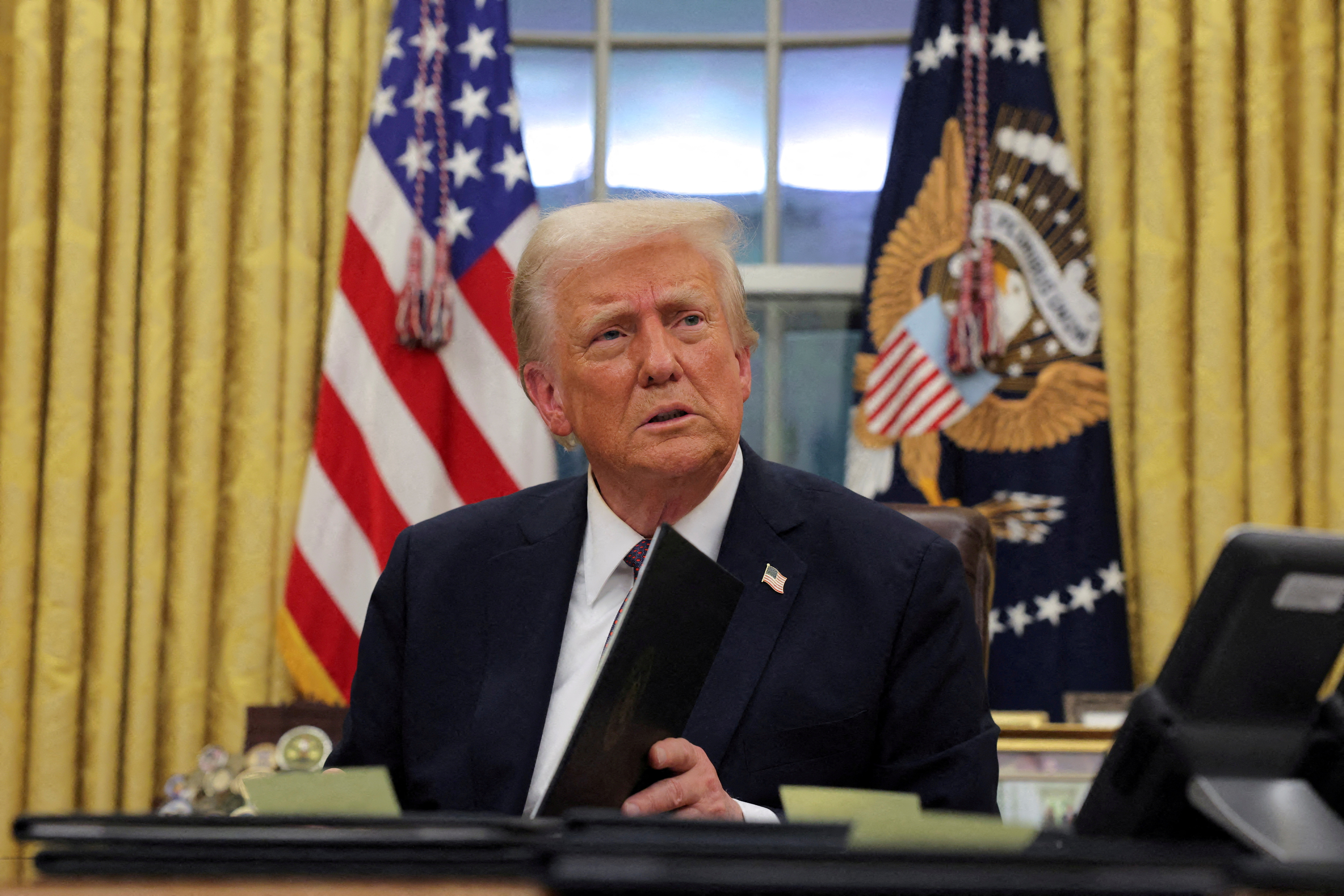 Donald Trump signs executive orders at his desk in the Oval Office.
