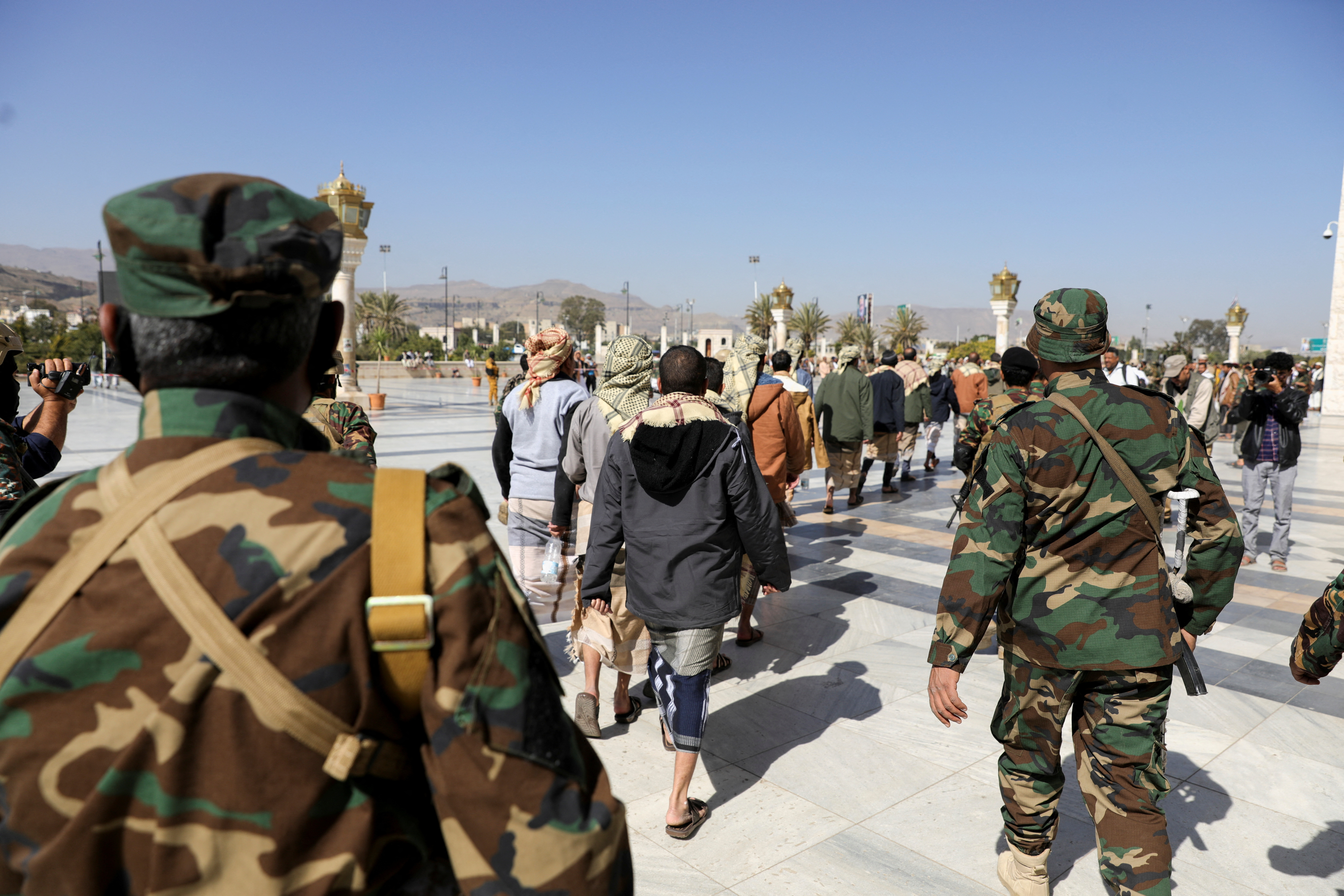 Houthi fighters walk next to detained people
