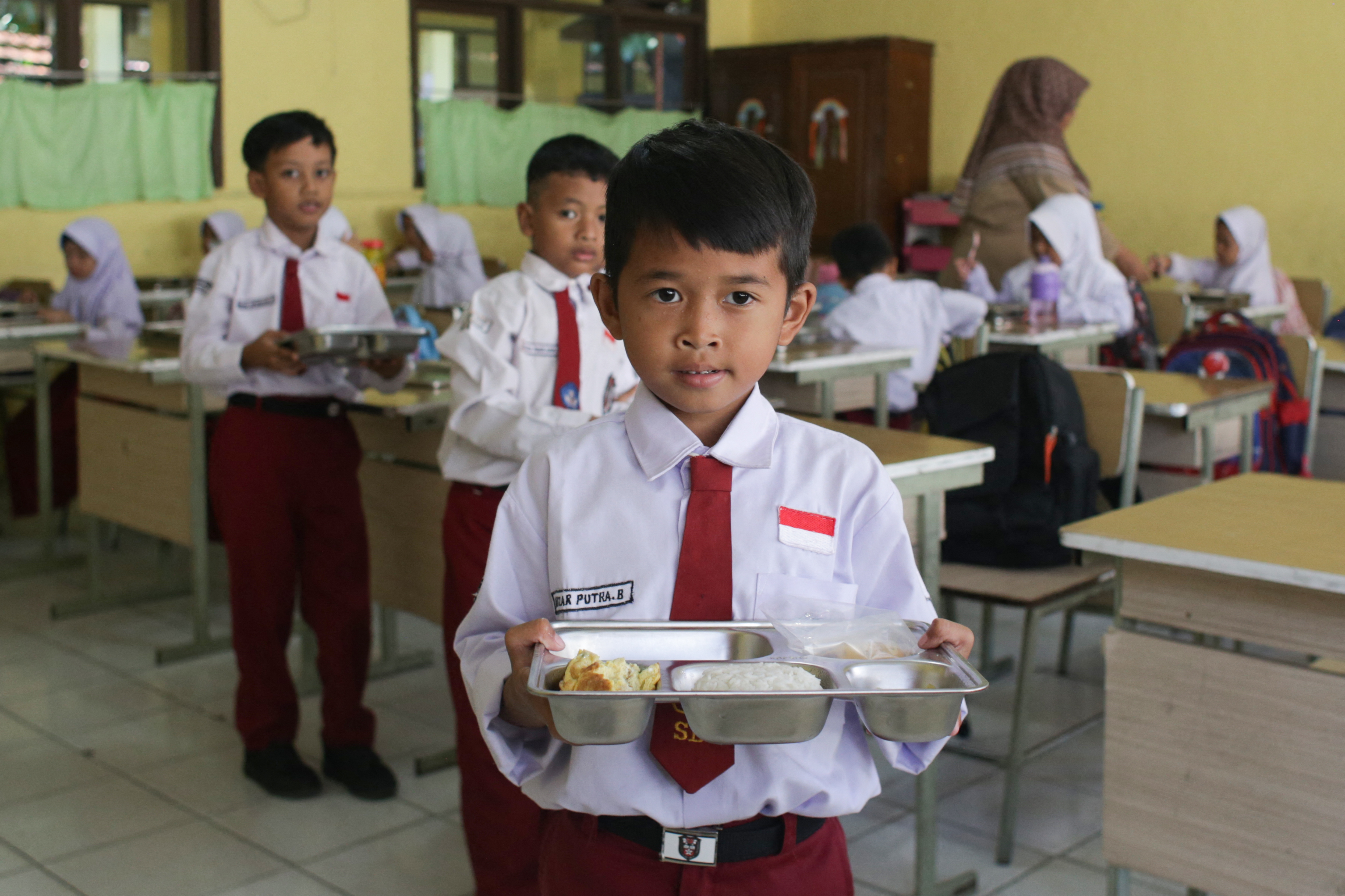 Students receive lunch plates on the first day of a free-meal programme at Kedung Badag 1 State Elementary School in Bogor, West Java, on January 6