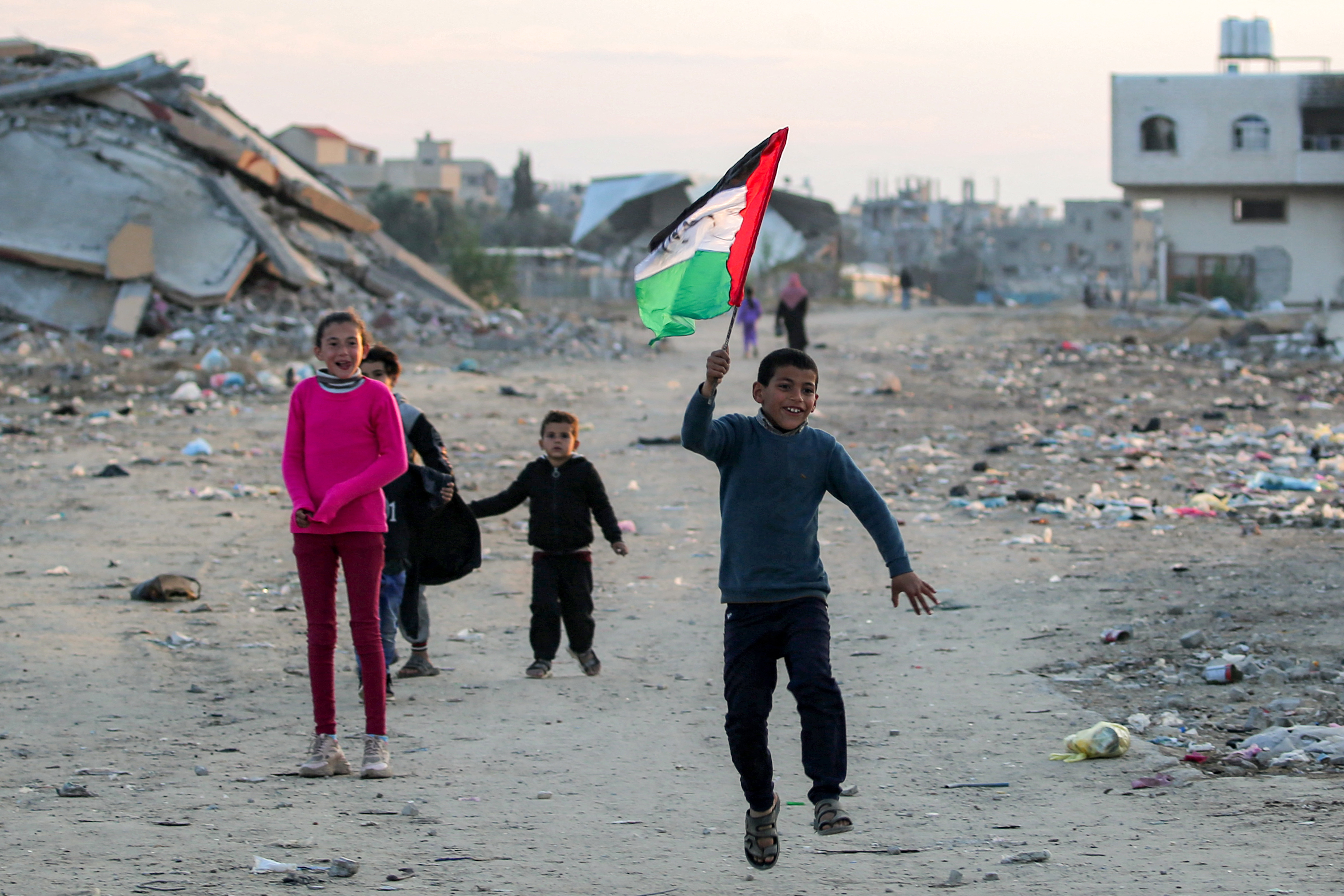 A boy runs with a Palestinian flag inscribed with the Arabic phrase "we sacrifice ourselves for the nation", at a camp for people displaced by conflict in Bureij in the central Gaza Strip on January 17, 2025 following the announcement of a truce amid the ongoing war between Israel and Hamas. (Photo by Eyad BABA / AFP)