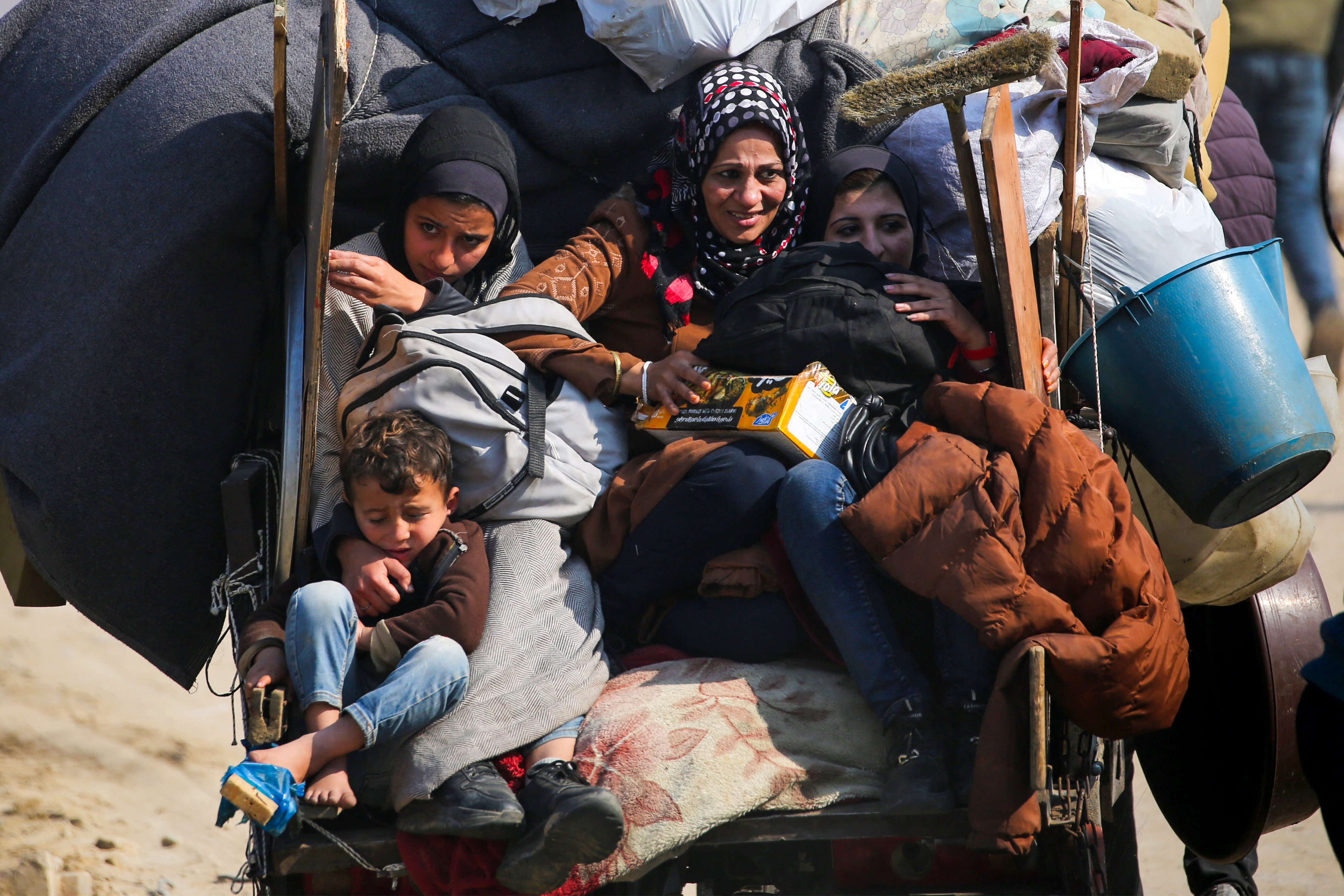 A displaced family rides on the back of a vehicle with their belongings