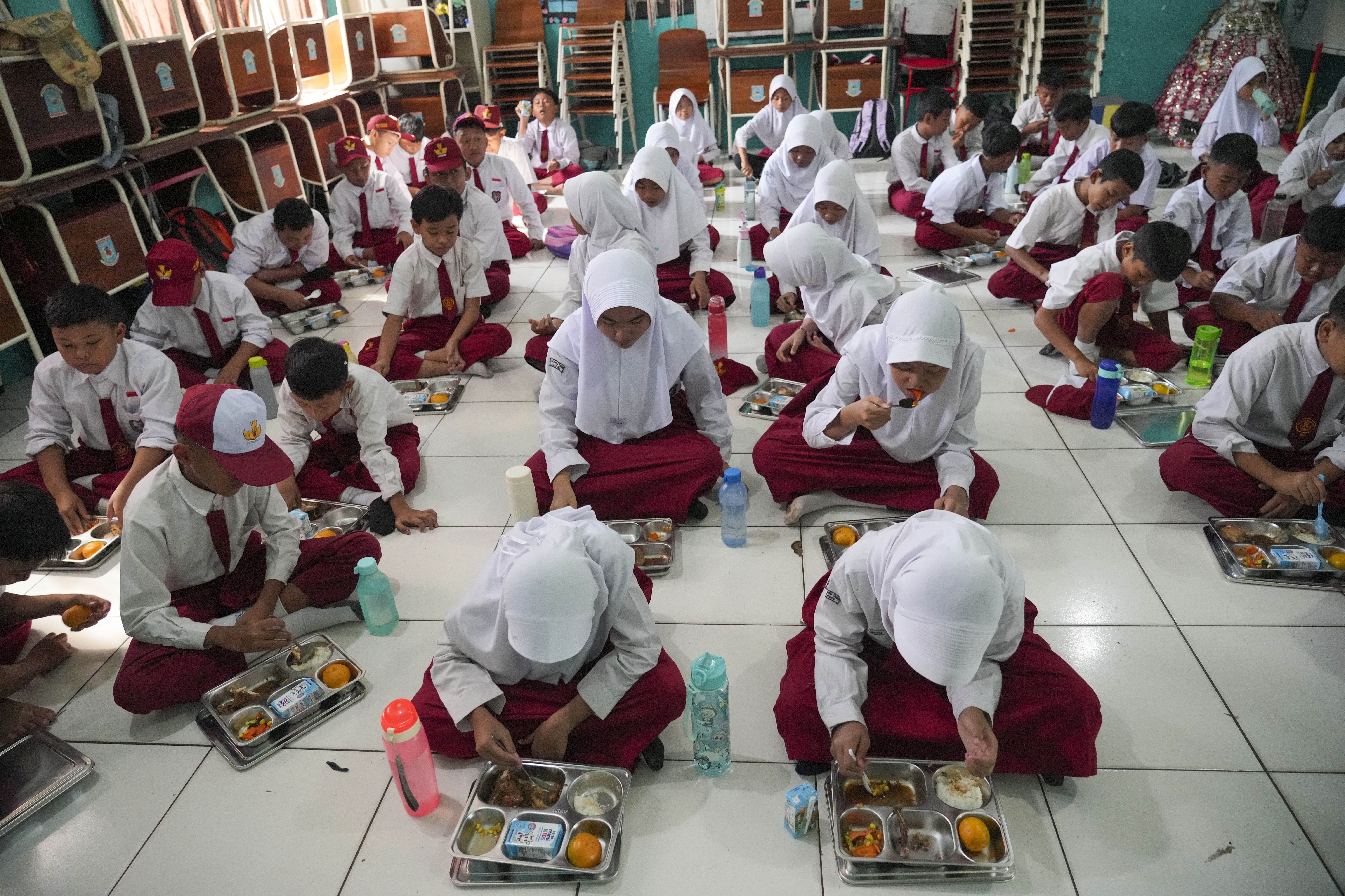 Students sit on the floor as they have their meals during the kick off of President Prabowo Subianto's ambitious free meal program to feed children and pregnant women nationwide despite critics saying that its required logistics could hurt Indonesia's state finances and economy, at an elementary school in Banten