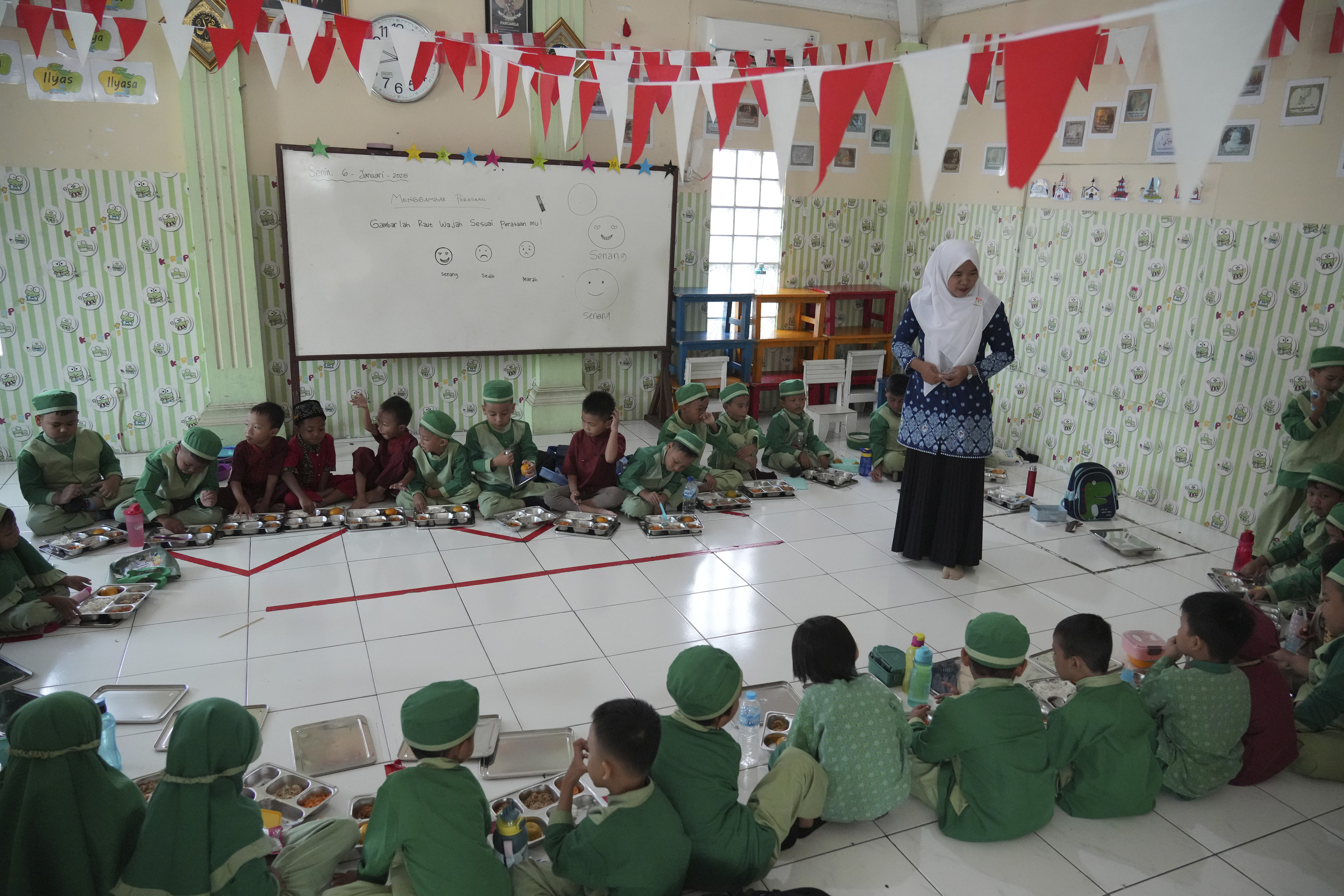 Students sit on the floor as they have their meals during the kick off of President Prabowo Subianto's ambitious free meal program to feed children and pregnant women nationwide despite critics saying that its required logistics could hurt Indonesia's state finances and economy at Early Childhood Education and Development in Jakarta, Indonesia, Monday