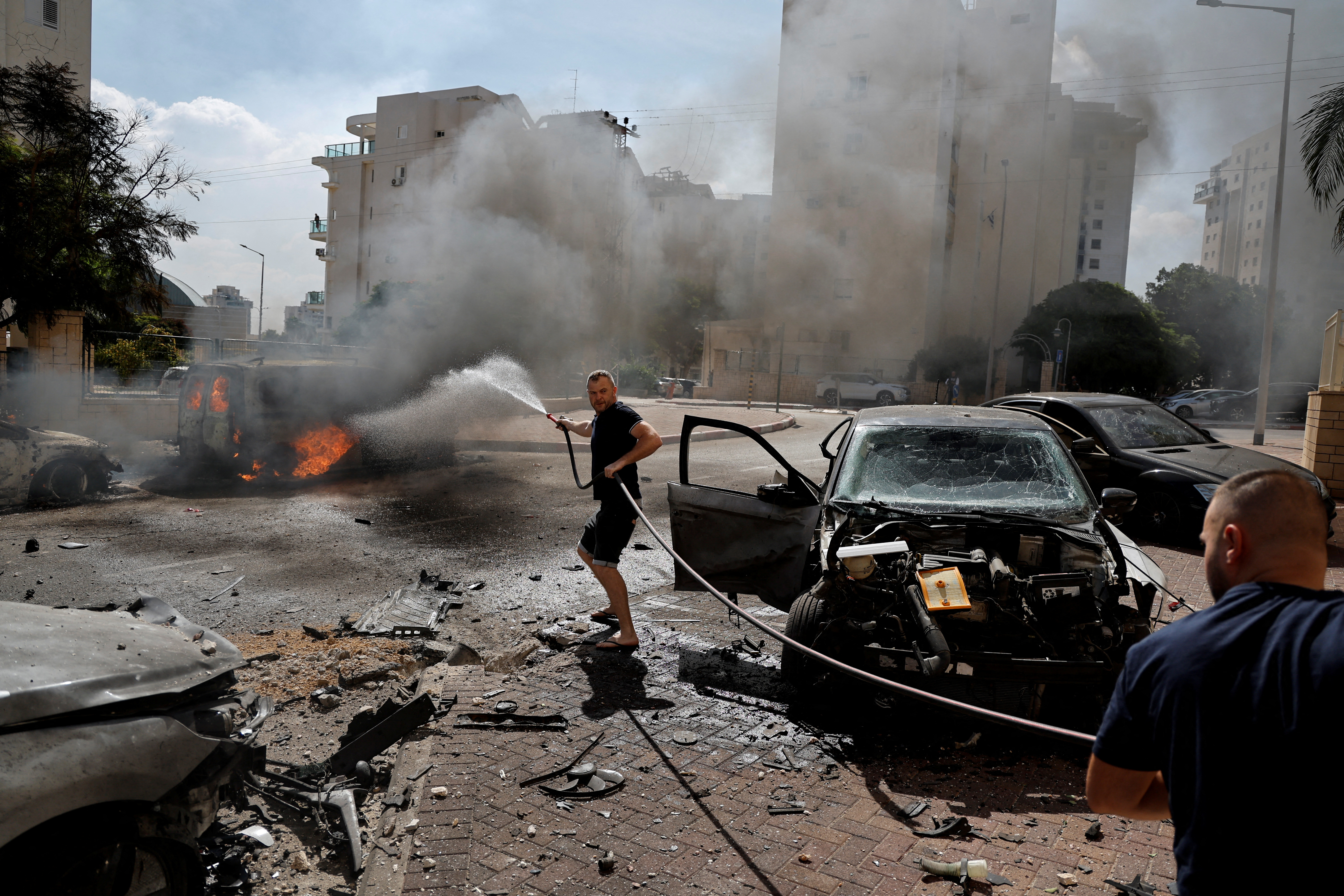 A man works to put out a fire engulfing a van, as rockets are launched from the Gaza Strip.