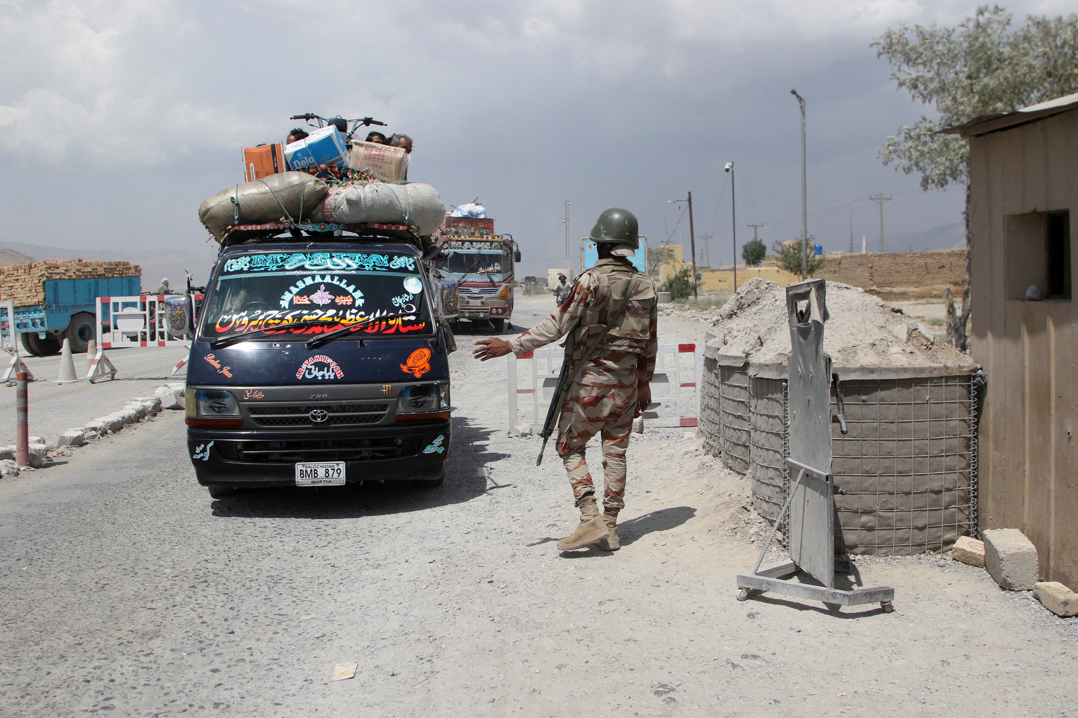 A paramilitary soldier stops and checks passenger vehicles at a security check post.