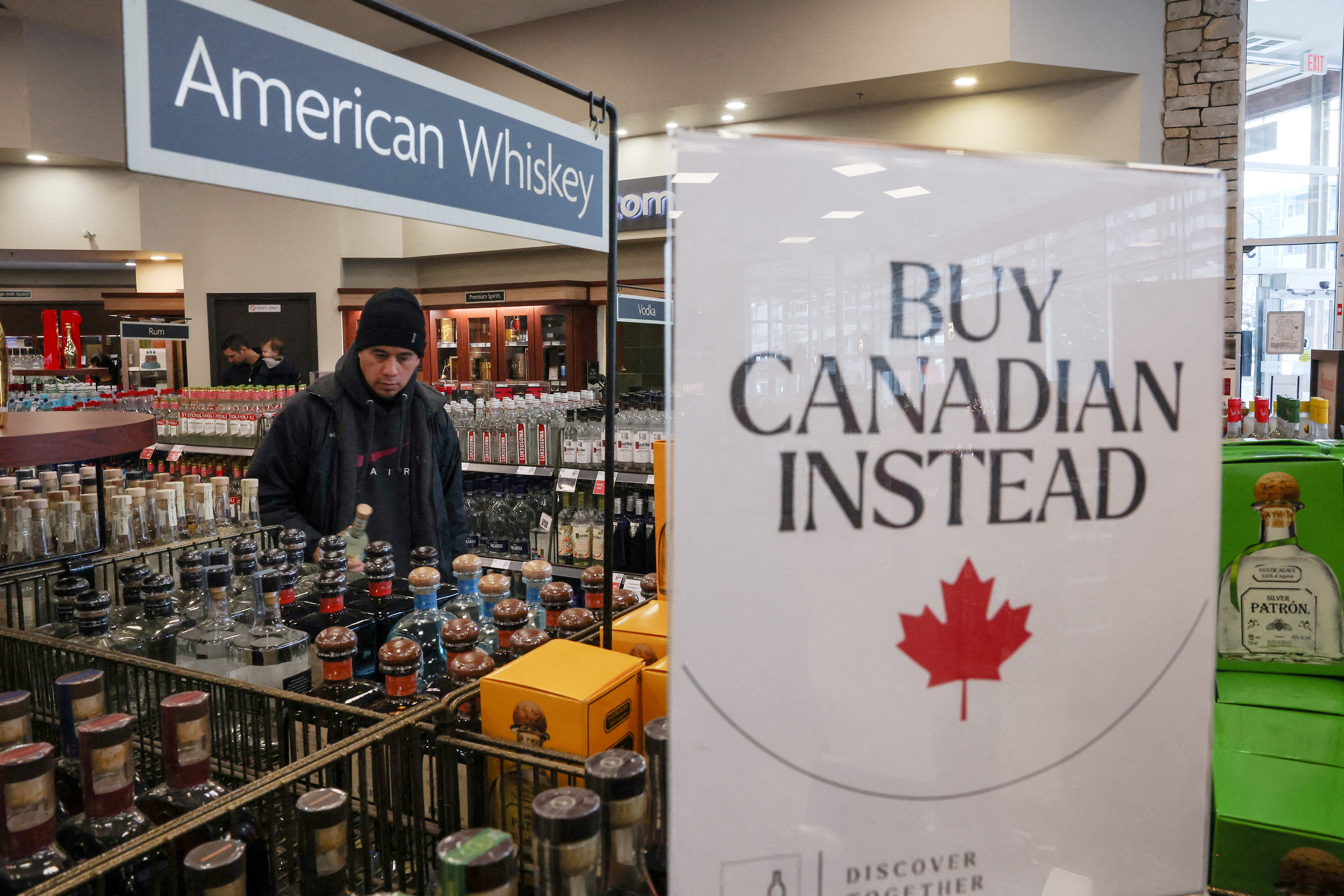 A customer stands behind a sign that reads 'Buy Canadian Instead' at a liquor store in British Columbia, Canada