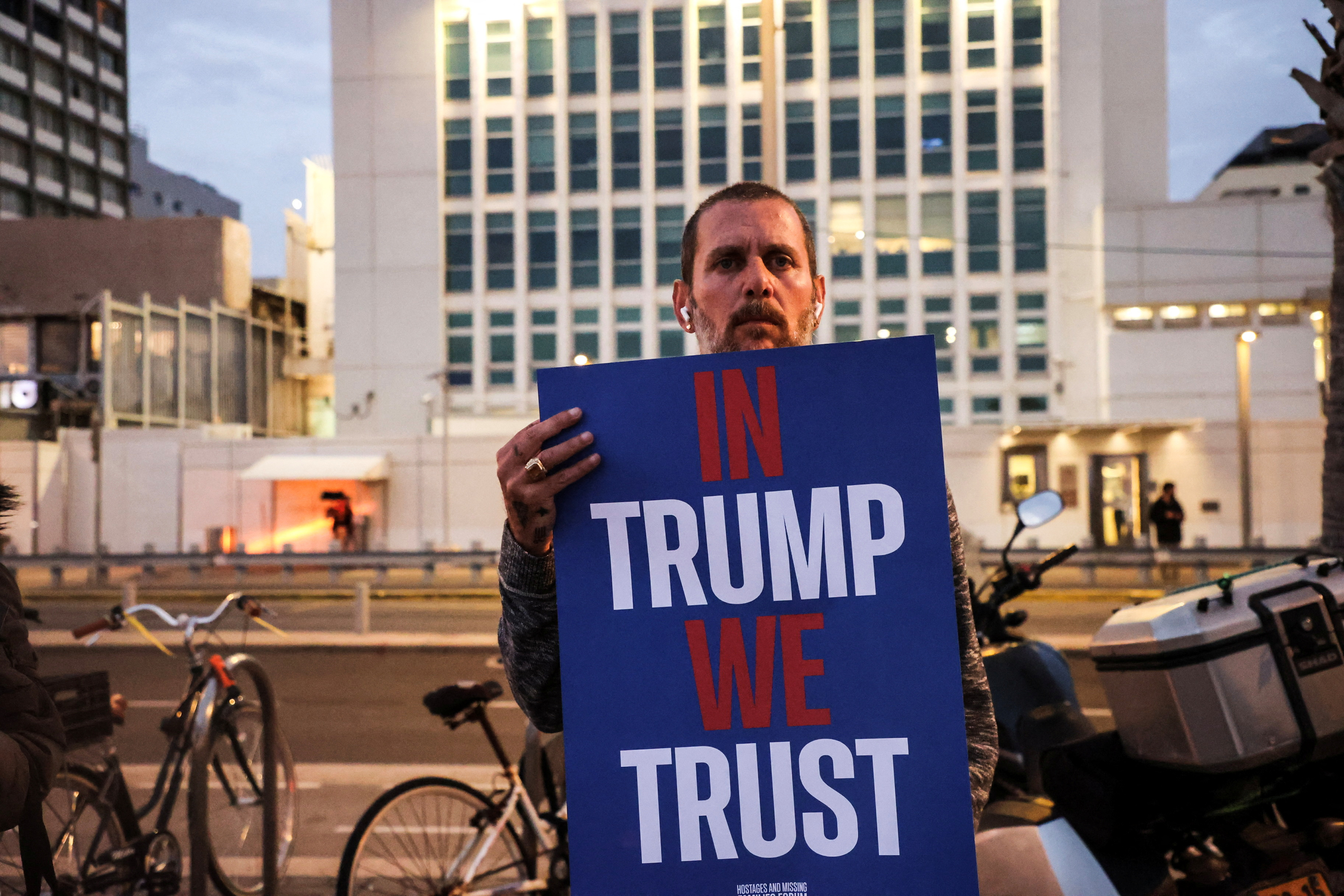 A man holds a sign that reads, 'In Trump we trust'
