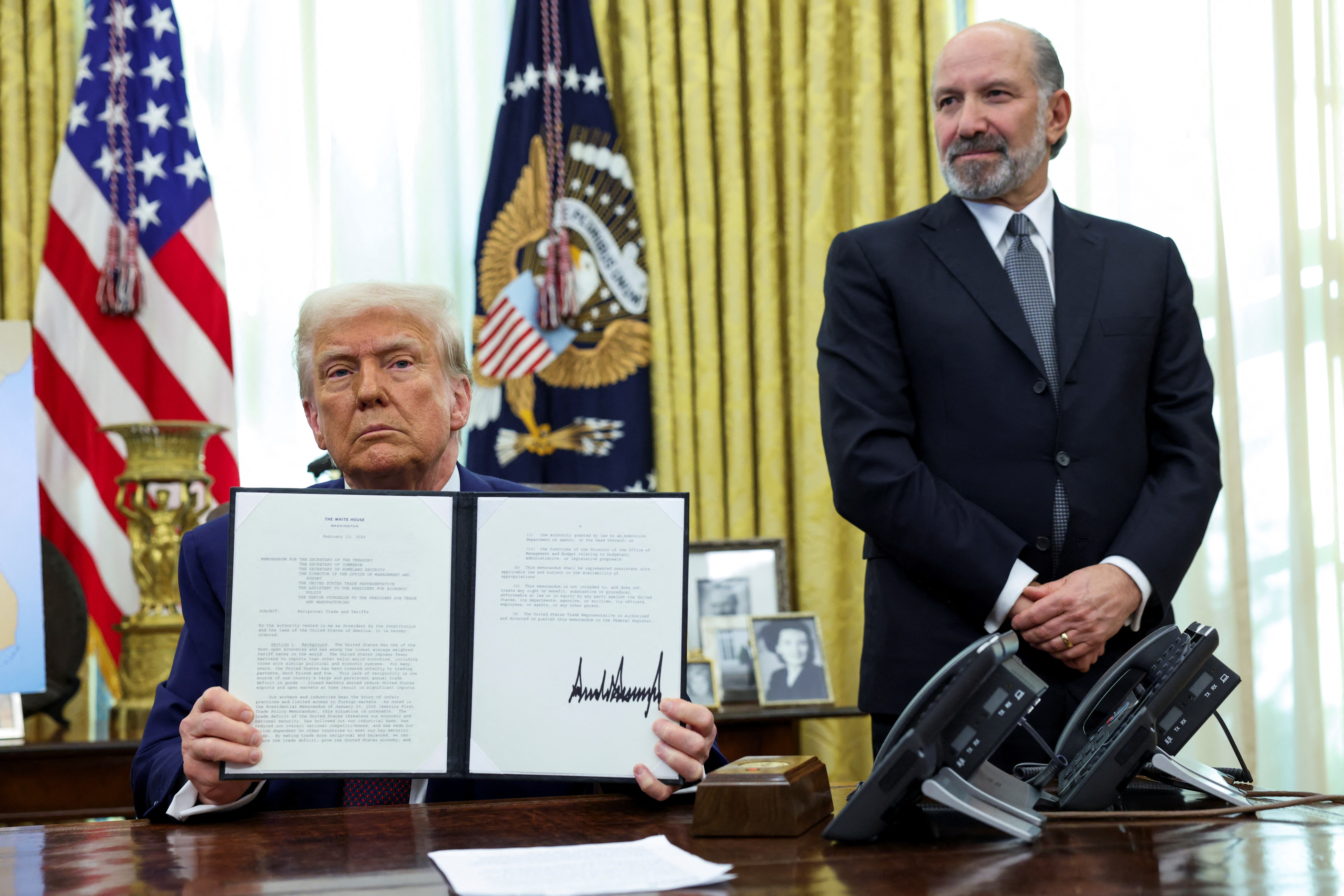 Trump holds up a memorandum next to Lutnick
