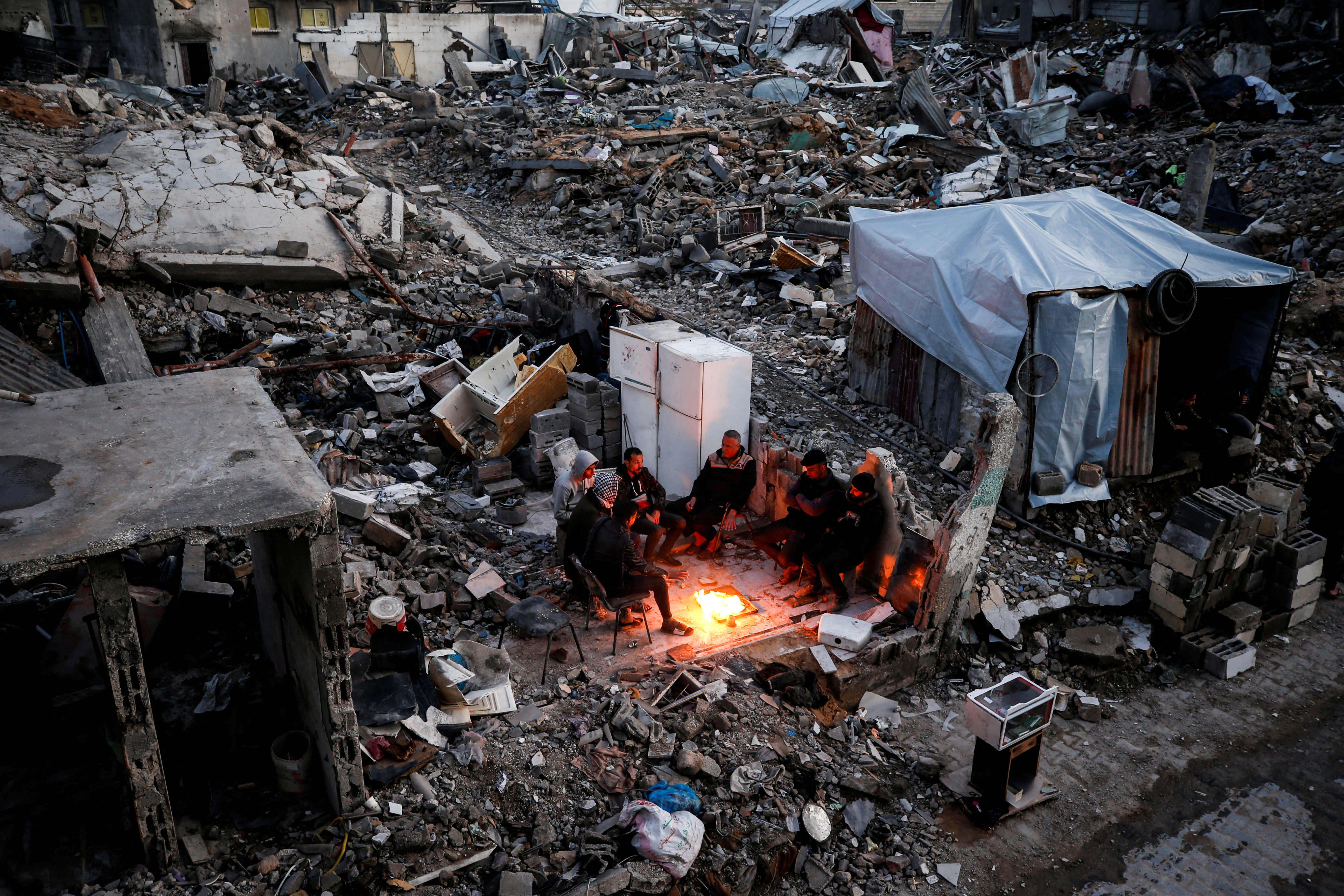 Palestinians gather near a fire next to the rubble of destroyed buildings, amid a ceasefire between Israel and Hamas, at Jabalia refugee camp, northern Gaza Strip