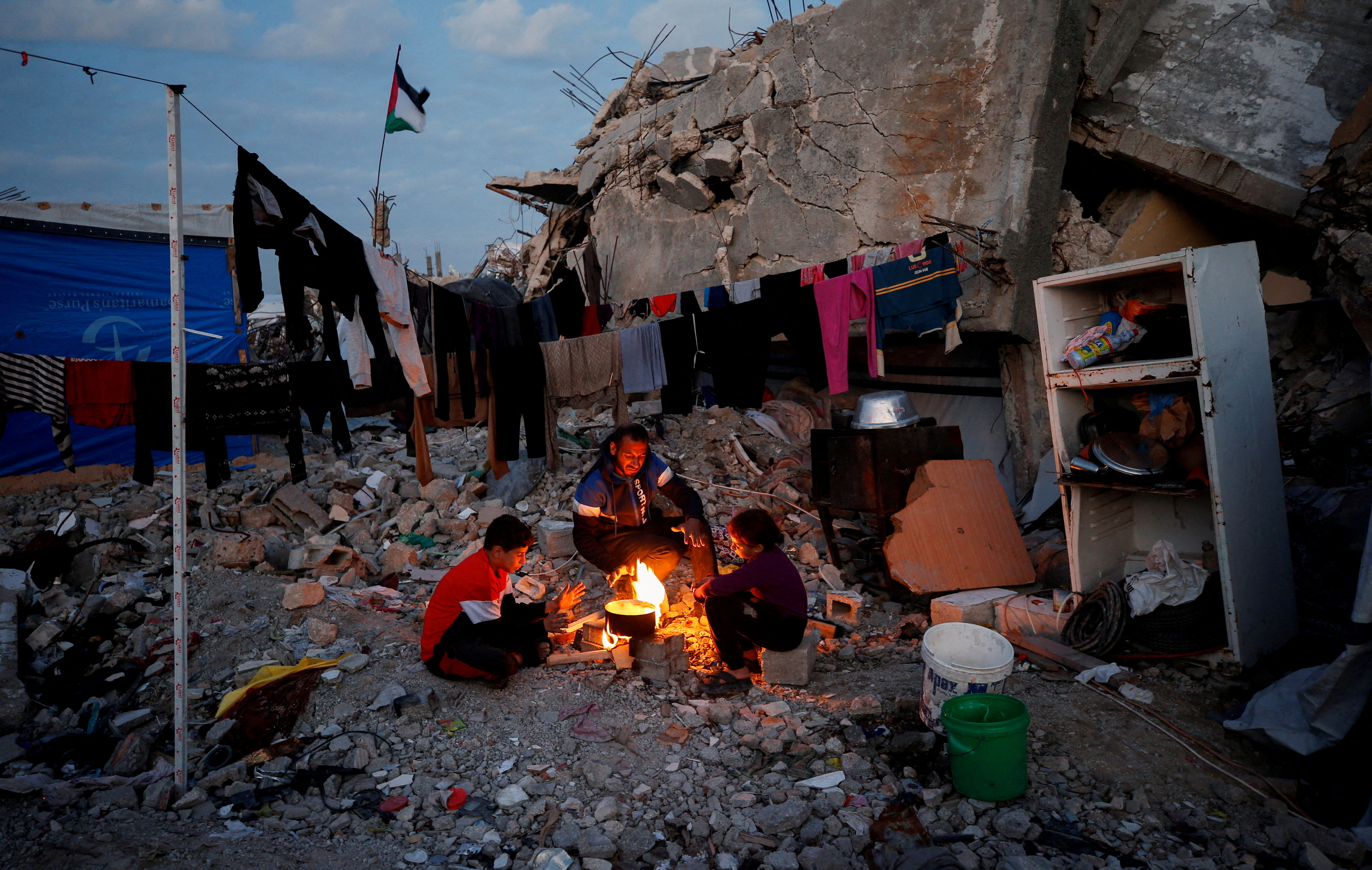 Palestinians sit around a fire amid destruction in Gaza