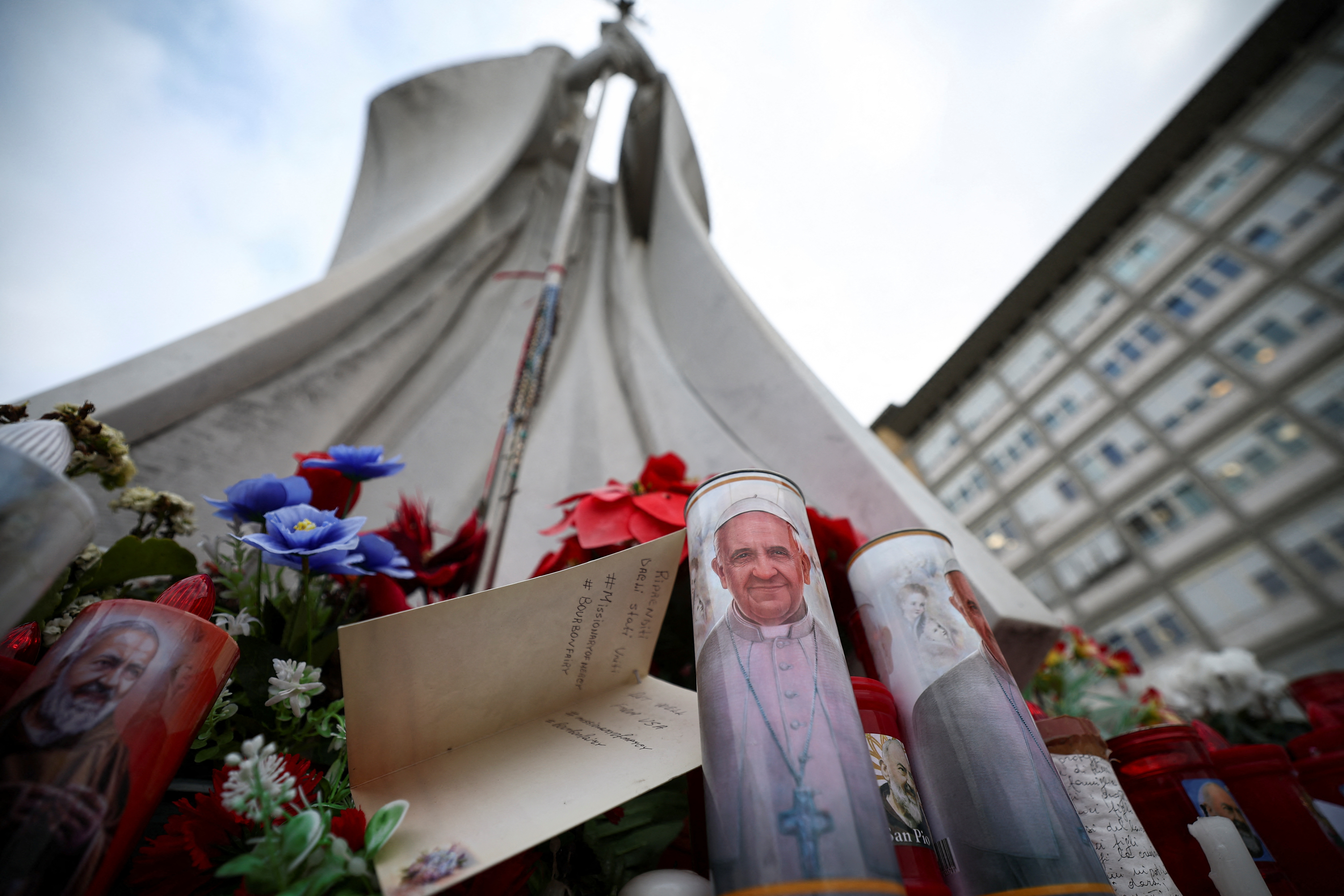 A candle with an image of Pope Francis and a card lie near the statue of the late Pope John Paul II outside the Gemelli Hospital
