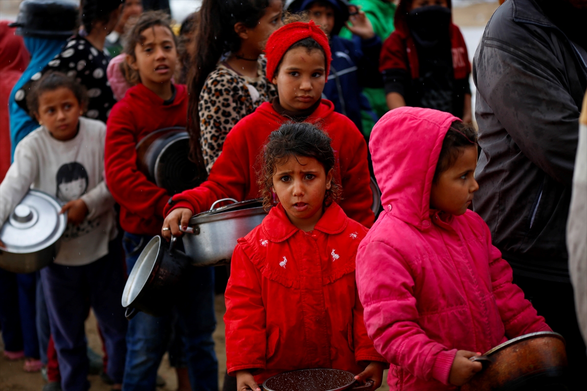 children stand in a line holding pots to receive food with