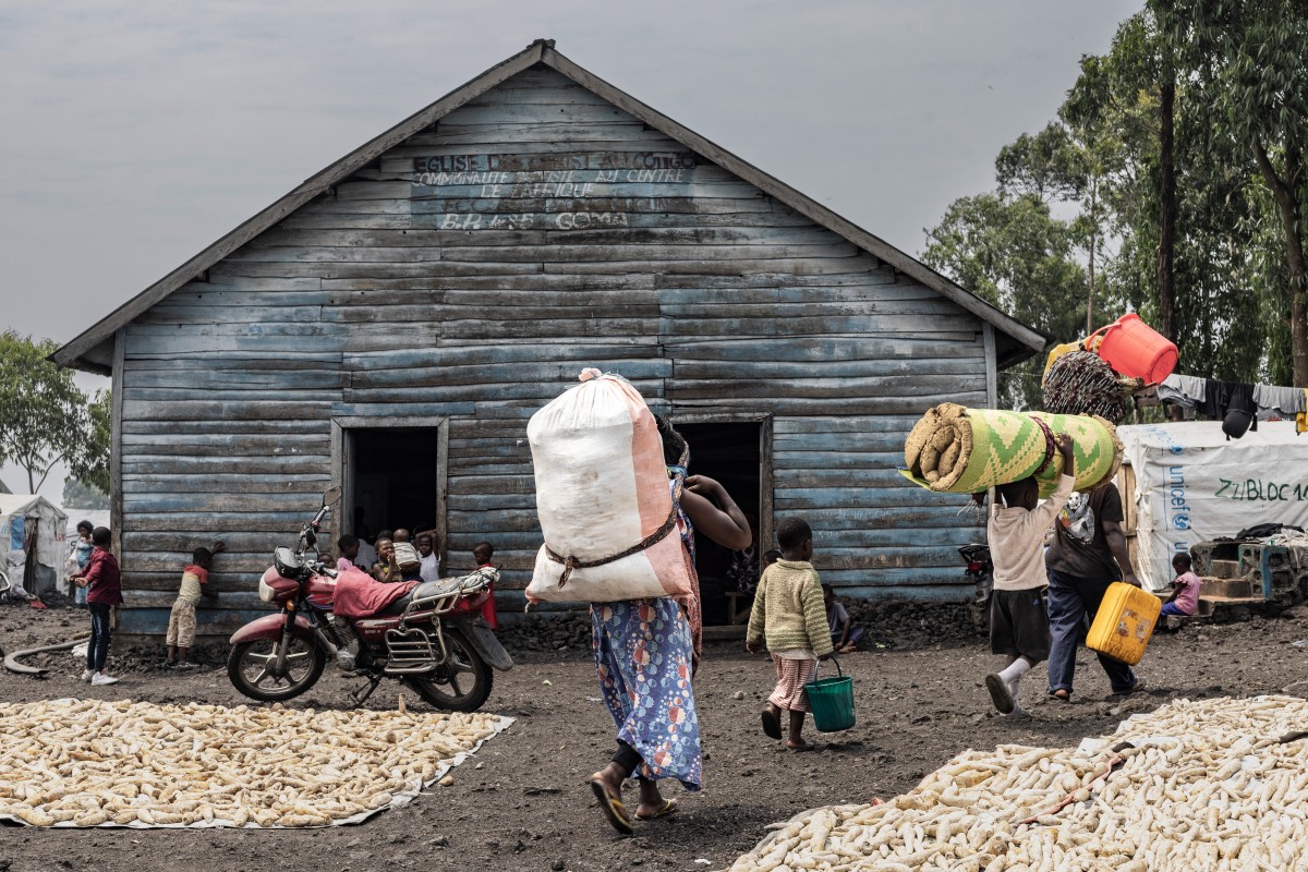 Internally displaced residents carry some of their belongings as they walk past the CBCA Mugunga Church, located at the Mugunga IDP camp in Goma