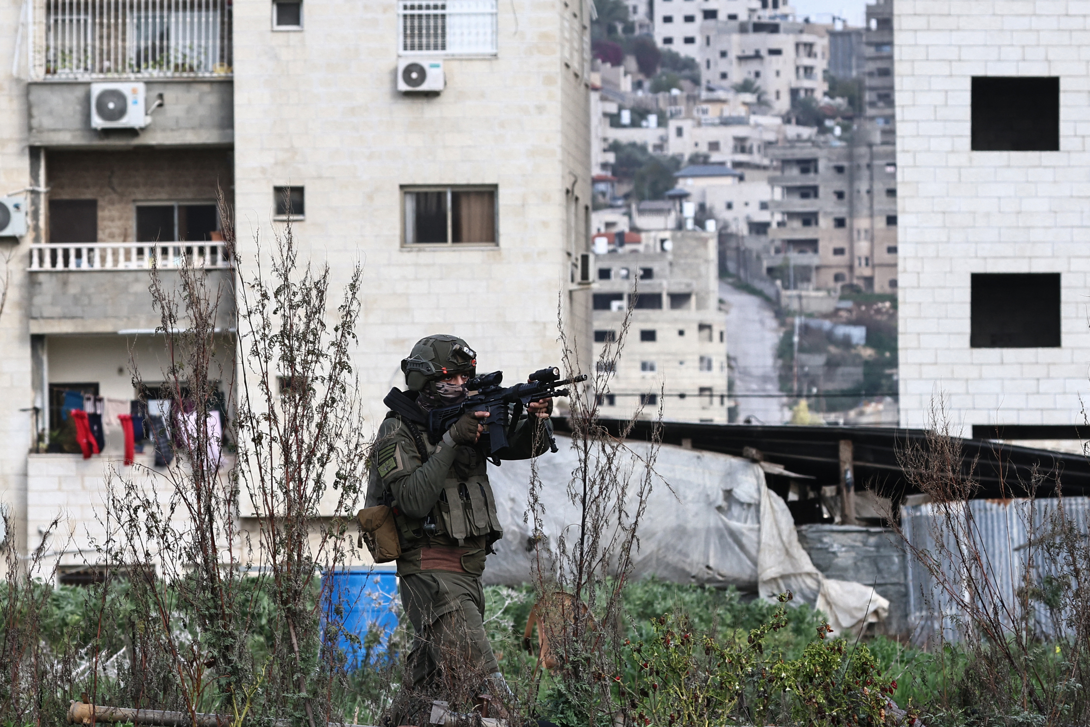 a solider points a gun near an apartment building