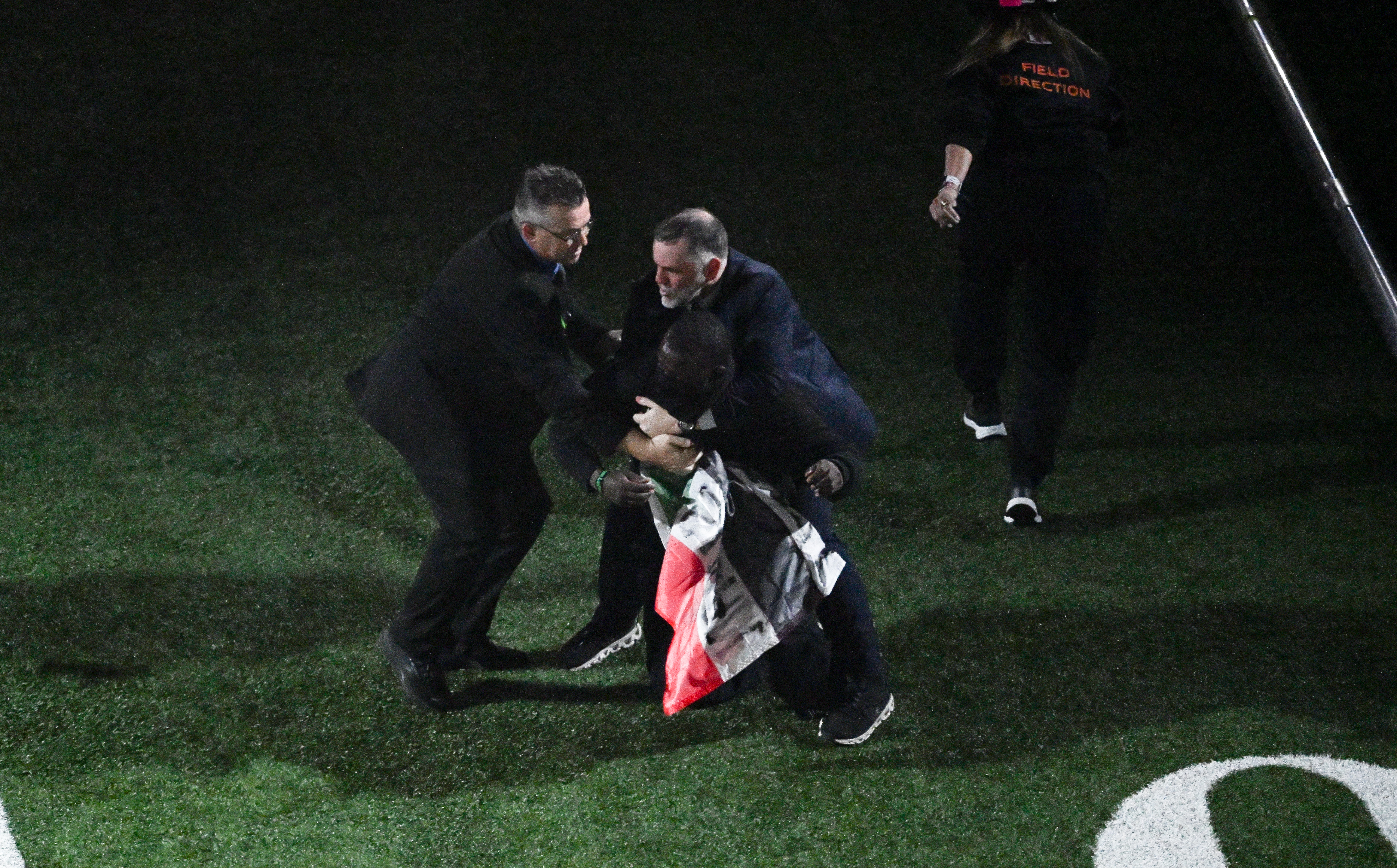 people in black uniforms wrestle a person with a flag to the grass
