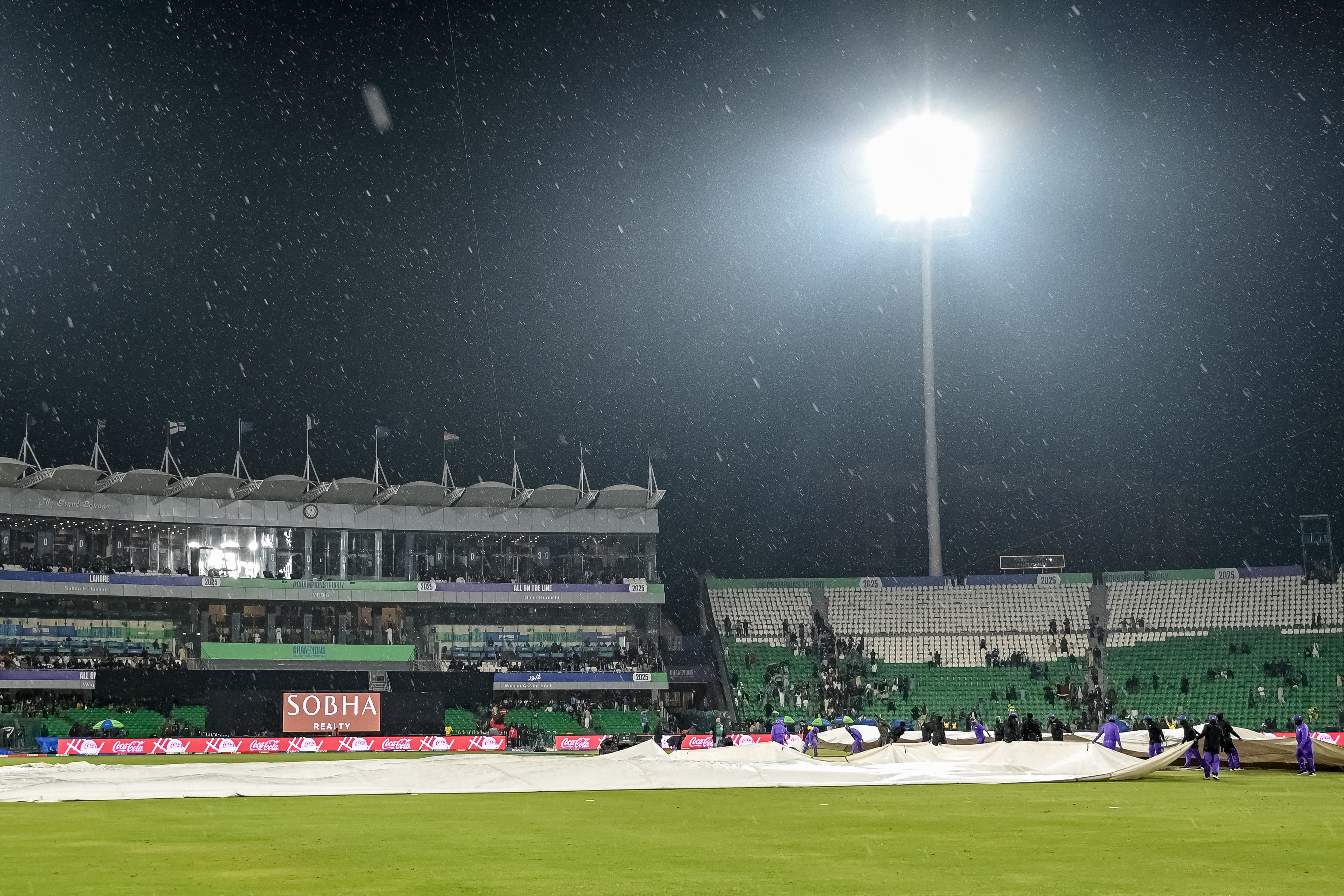 Groundmen cover the pitch as rain stops play during the ICC Champions Trophy one-day international (ODI) cricket match between Australia and Afghanistan at the Gaddafi Stadium in Lahore on February 28, 2025. (Photo by Aamir QURESHI / AFP)