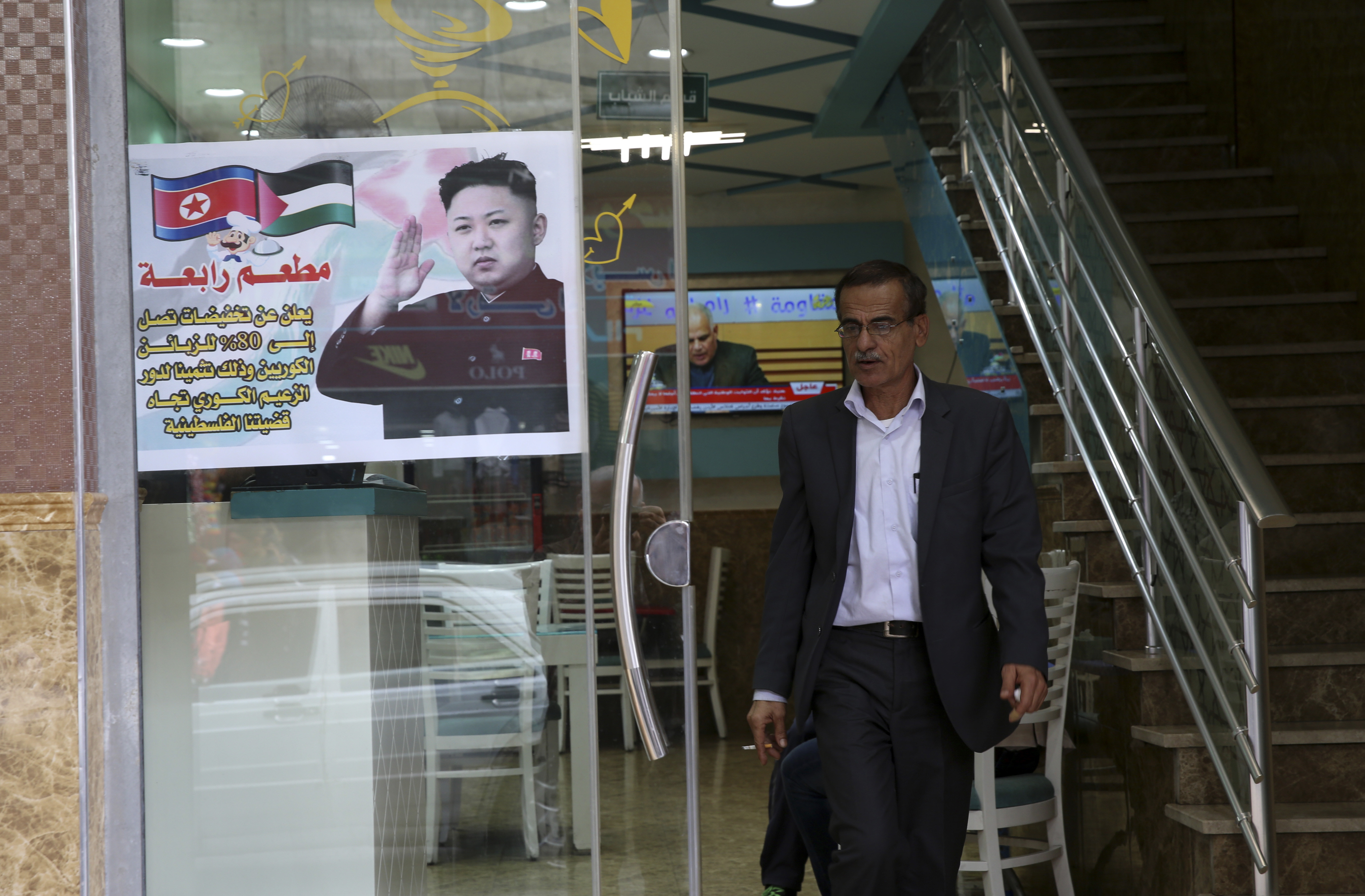 A Palestinian customer walks out of a shawarma restaurant with a poster of North Korean leader Jim Jong at the entrance of it in Jebaliya refugee camp, Gaza Strip, Thursday, Dec. 14, 2017. Arabic reads that " Raba restaurant announces 80% discount for Korean customers in appreciation of Korea's leader role toward the Palestinian cause". (AP Photo/Adel Hana)