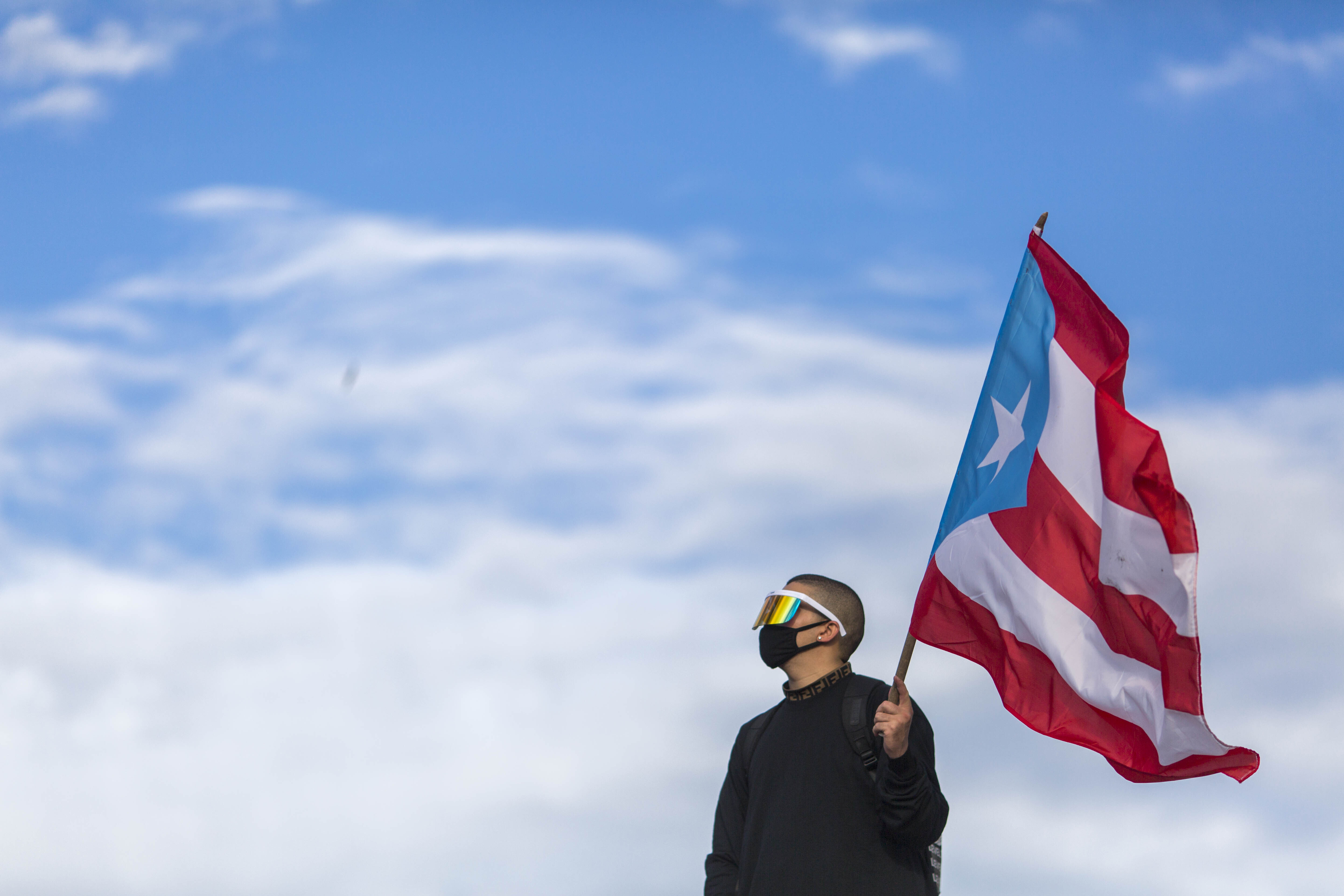 Latin trap and reggaeton singer Benito Antonio Martinez Ocasio, known by his stage name Bad Bunny, holds a Puerto Rican flag before a protest march against then-Governor Ricardo Rossello, in San Juan, Puerto Rico, July 17, 2019 [Dennis M Rivera Pichardo/AP Photo]