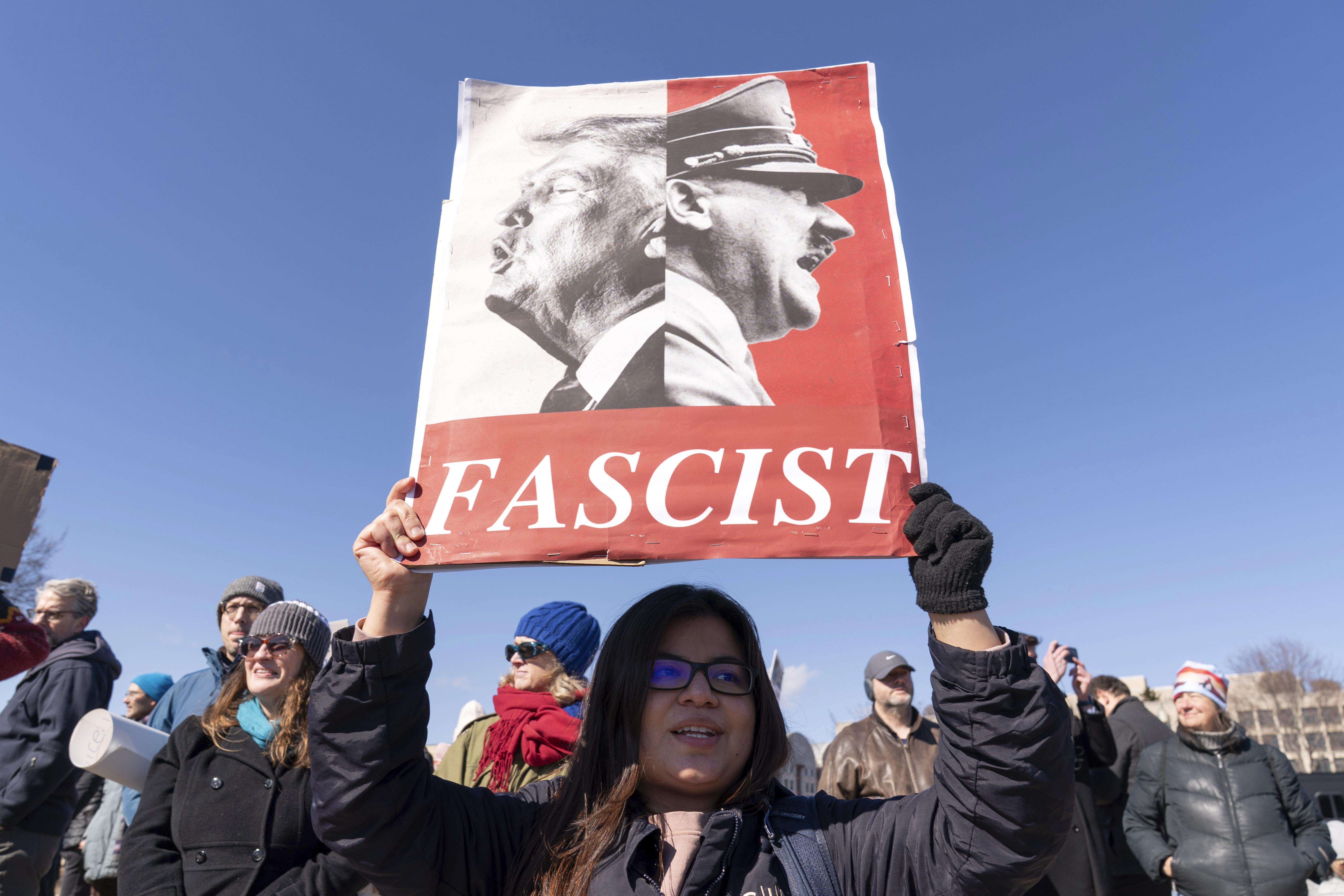 A protester holds up a sign that juxtaposes Trump with Hitler, above the word "fascist"