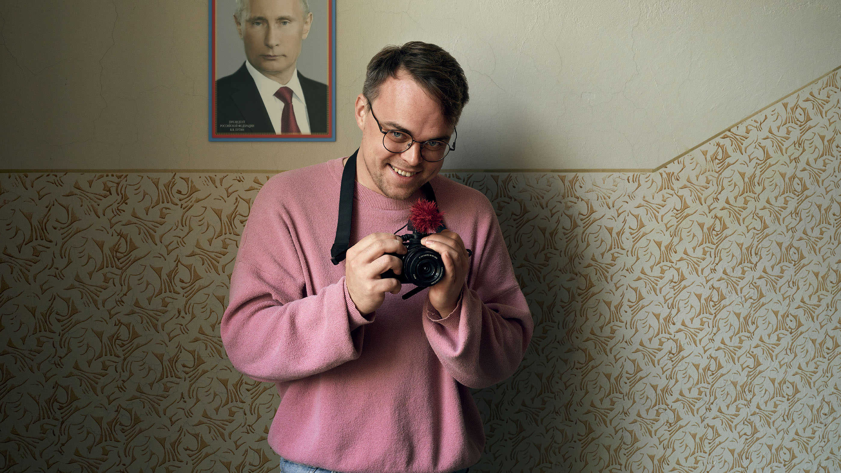 Pavel Talankin smiles as he looks down, holding his camera.