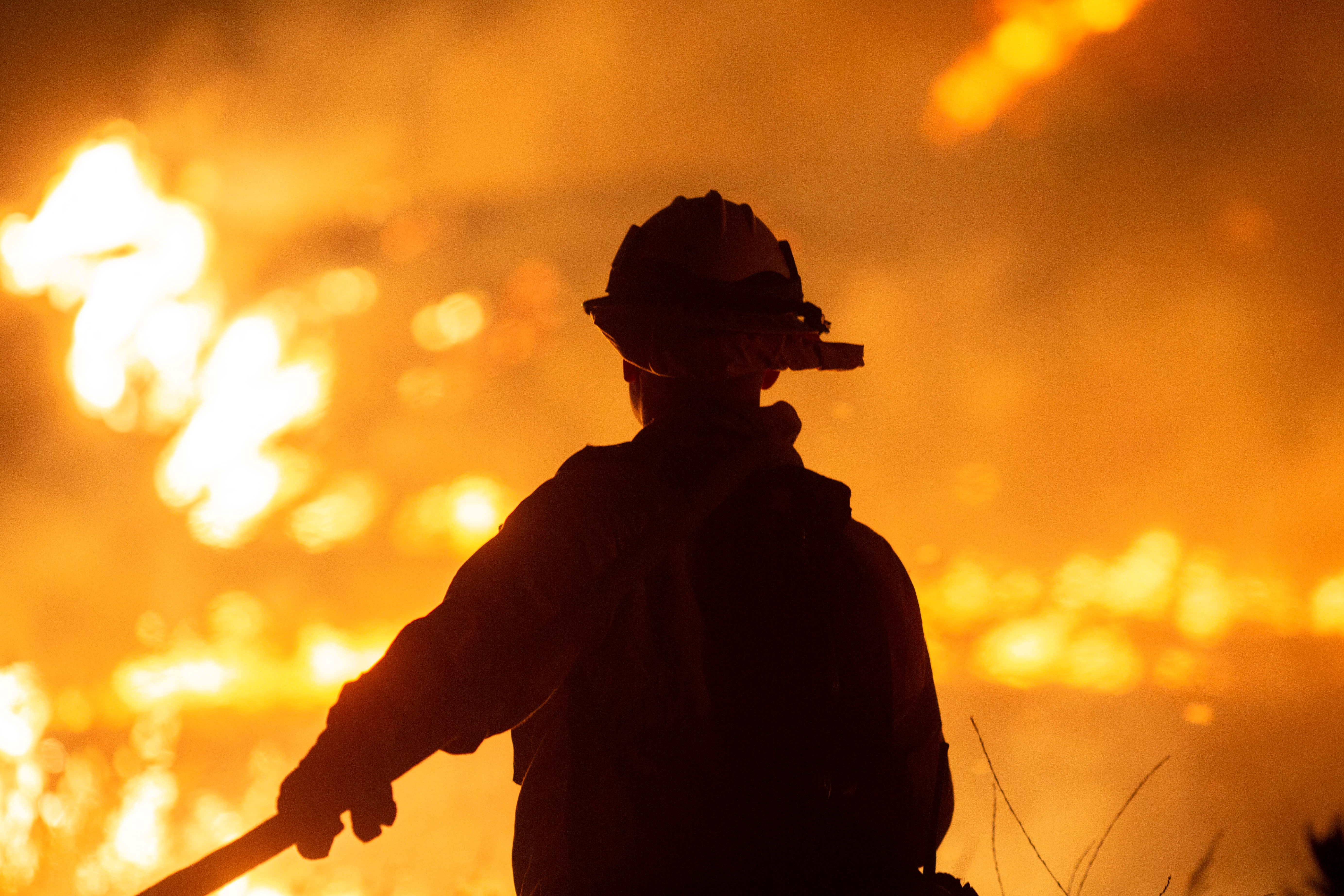 A firefighter stands in silhouette against nighttime flames
