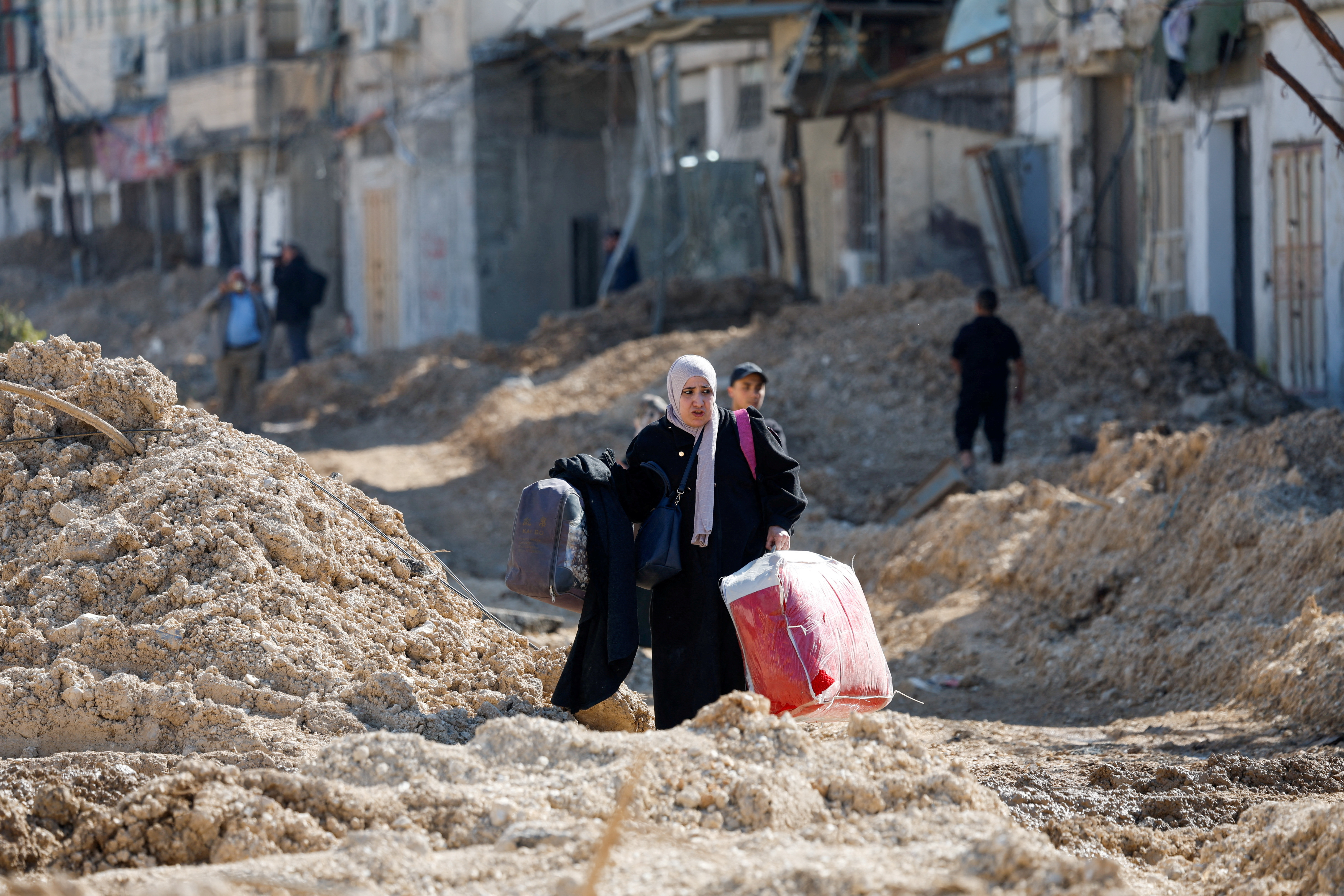 Palestinians walk on a damaged road, leaving Nur Shams refugee camp