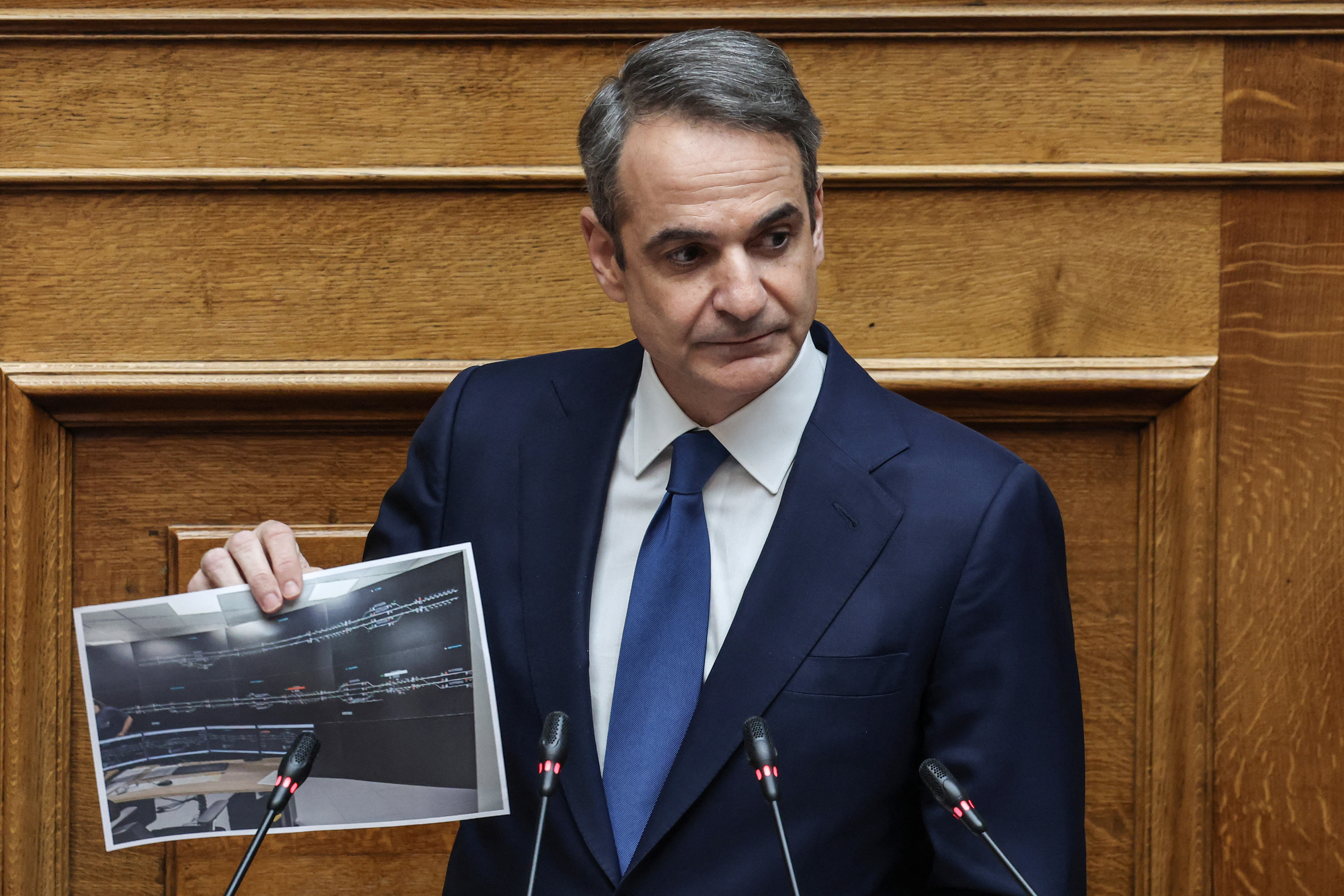 Greek Prime Minister Kyriakos Mitsotakis shows a picture during a debate on a 2023 train crash