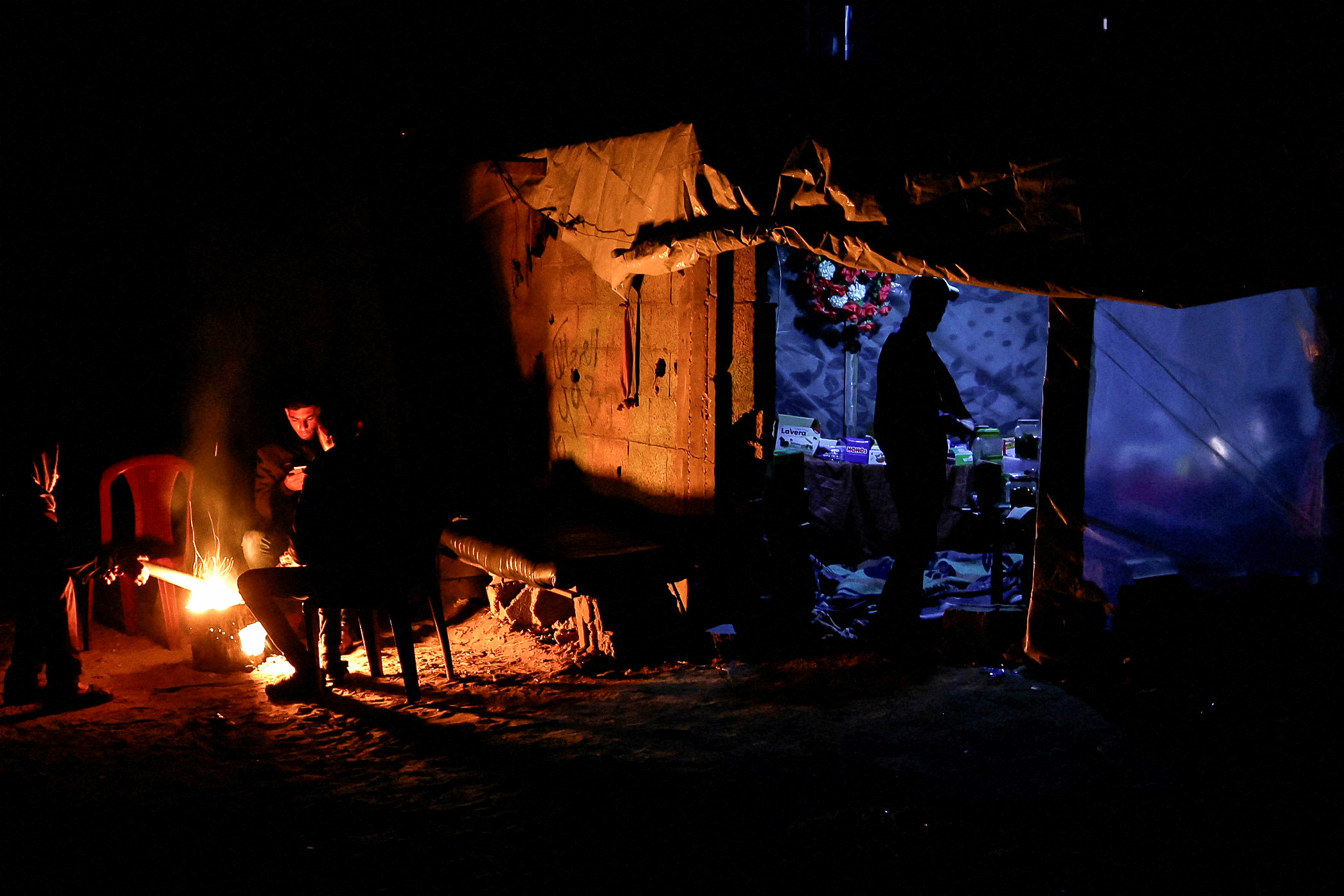Palestinians sit around a fire as a man stands at a makeshift shop during a power cut