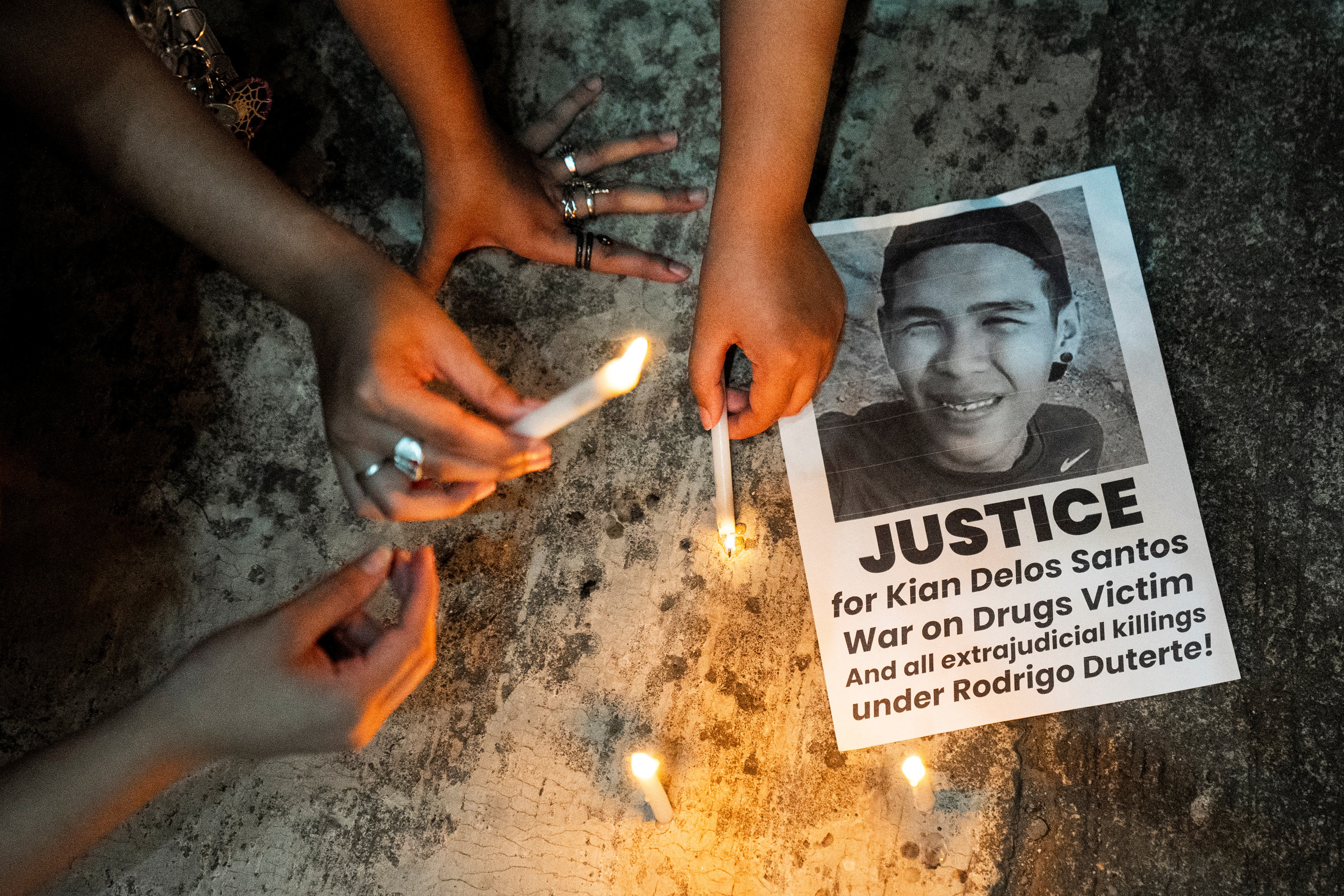 people light candles next to a black and white picture of a young man on a protest flyer