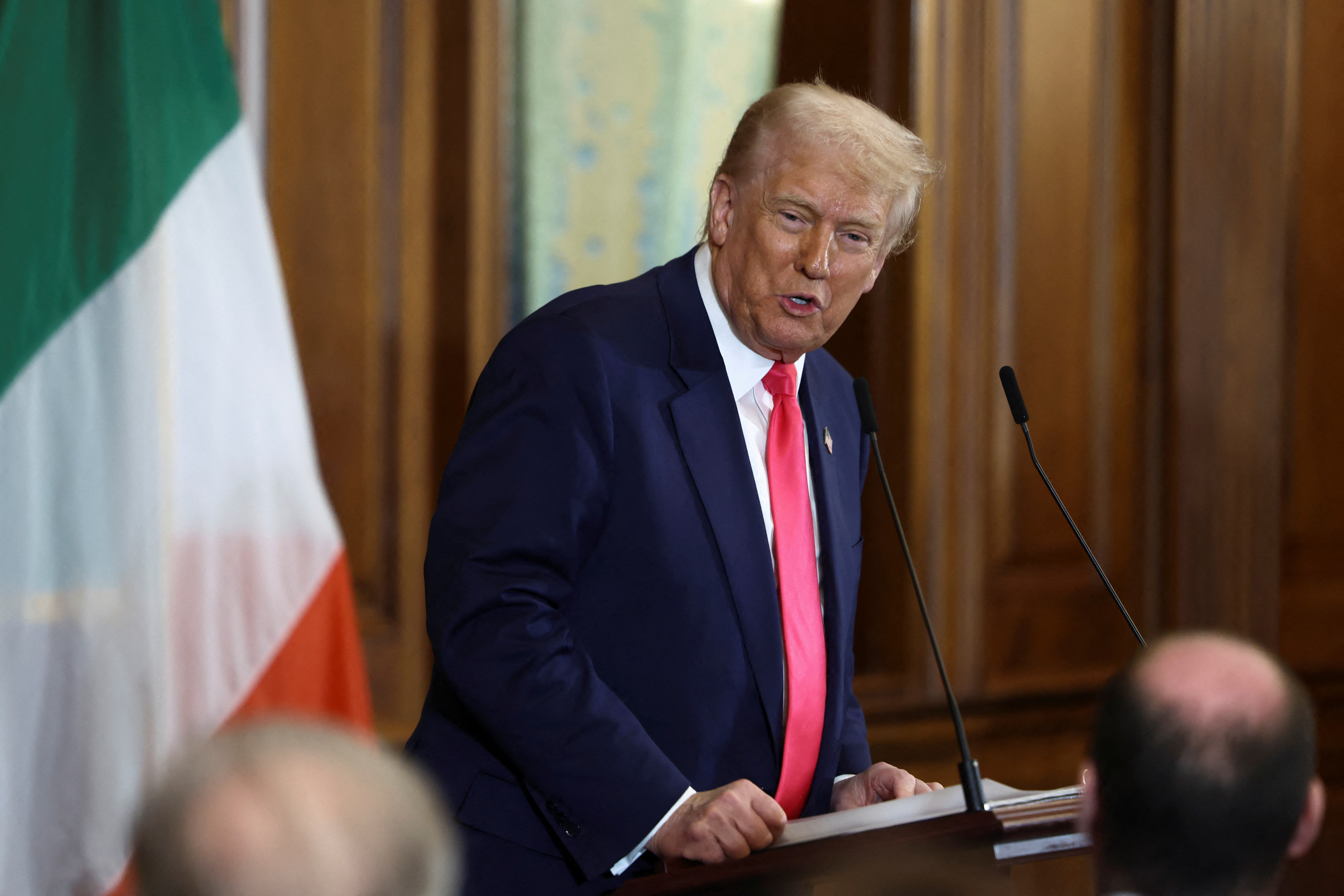 Donald Trump speaking at a podium next to an Irish flag.