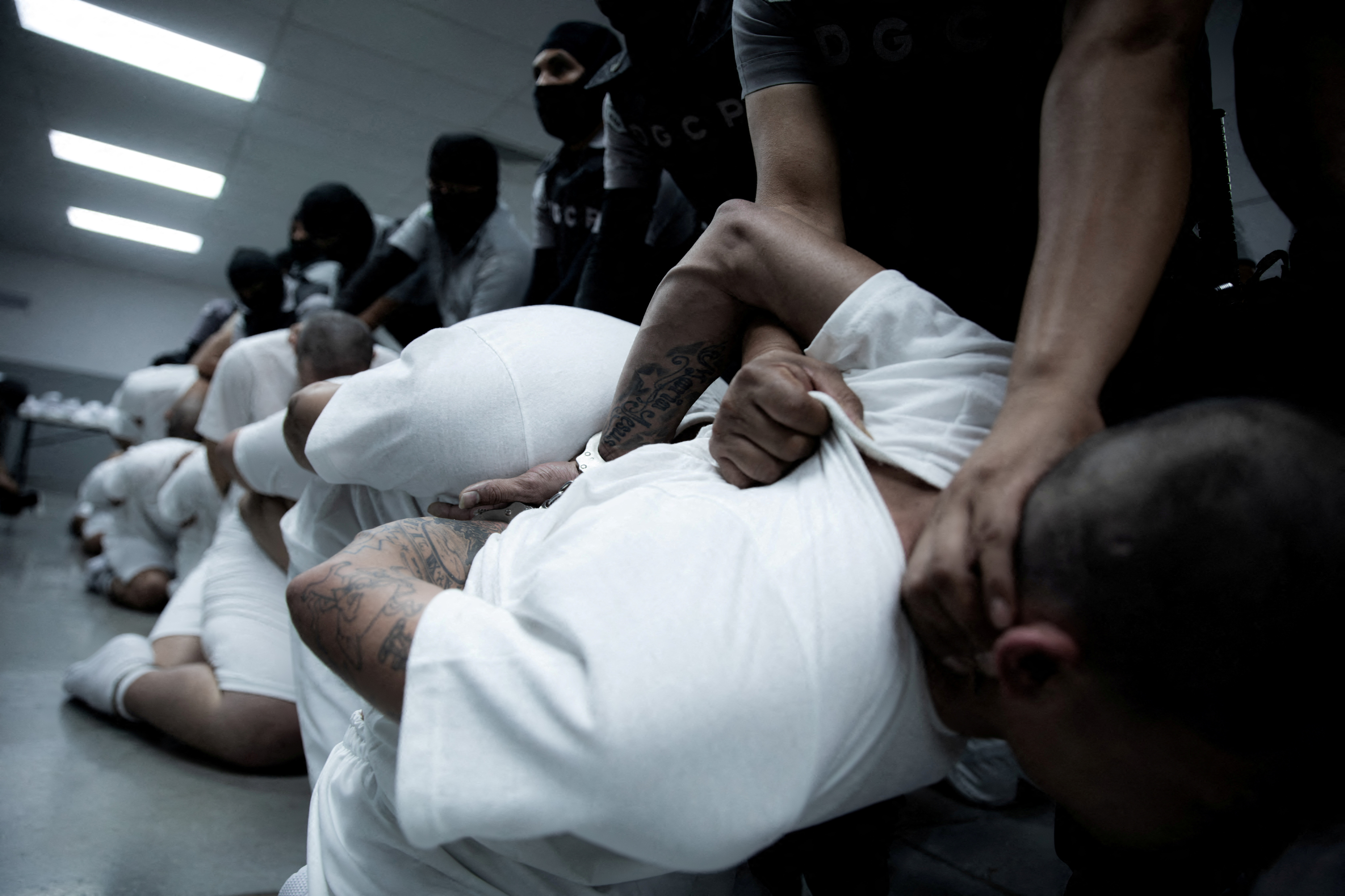 A handcuffed man deported from the US to El Salvador is held by a police officer