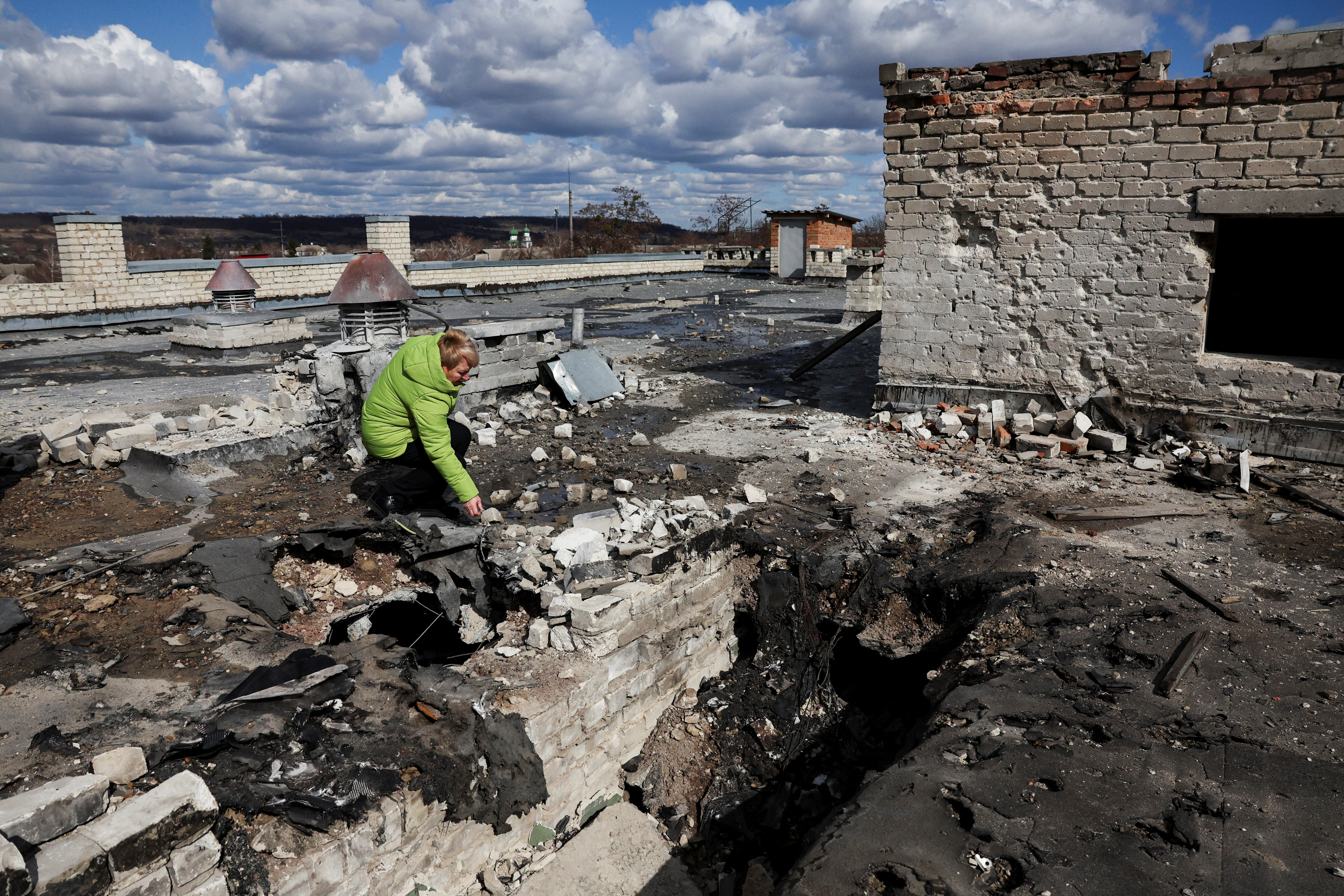 Olha Kyzym, Head of the Department of Education of the Pechenihy village council, picks up a piece of shrapnel of a Shahed drone on the rooftop of the village school, bombed two days prior in an overnight strike by three drones, amid Russia's attack on Ukraine, in Pechenihy, Ukraine, March 19, 2025. REUTERS/Violeta Santos Moura