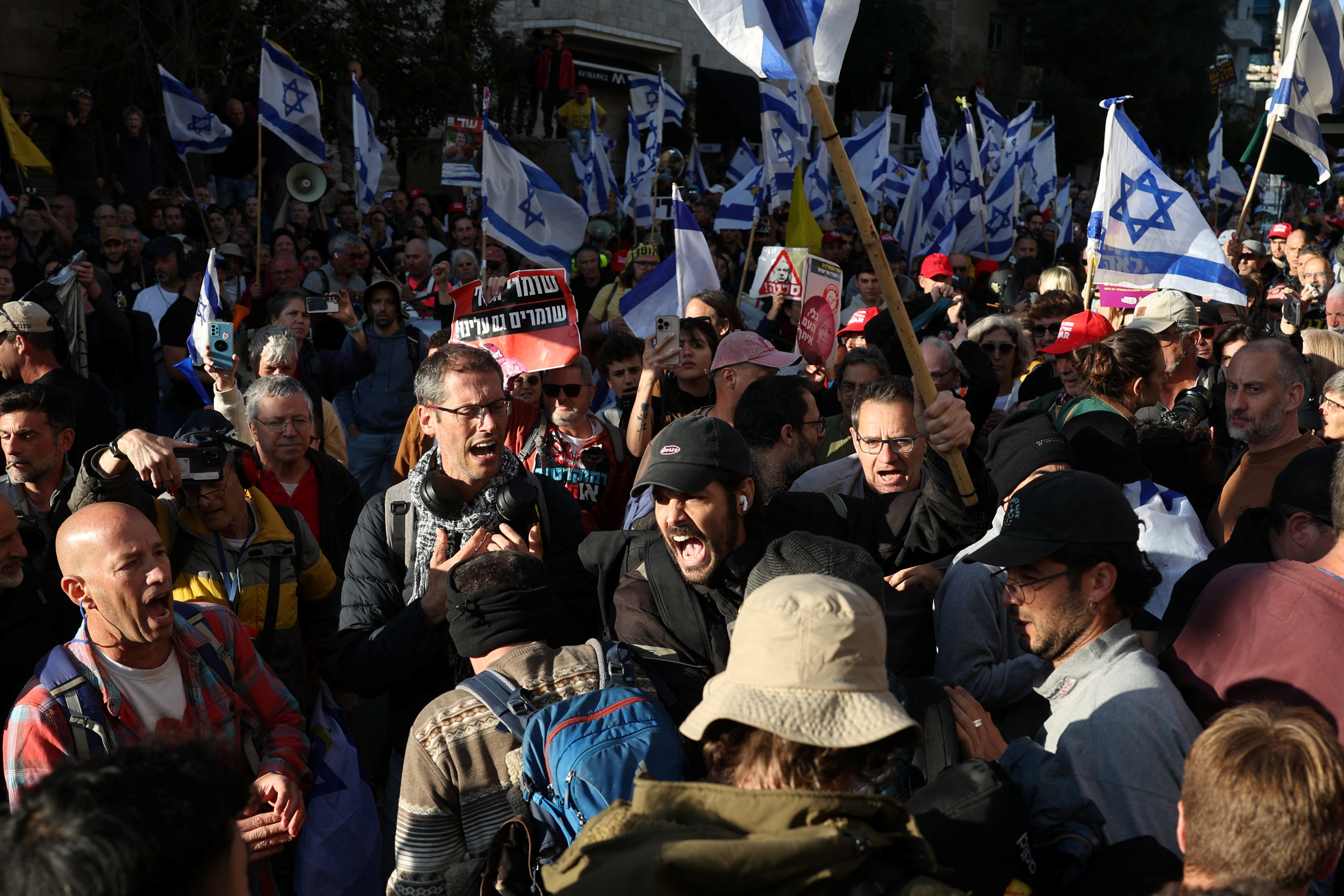 people wave israeli flags at a protest at night