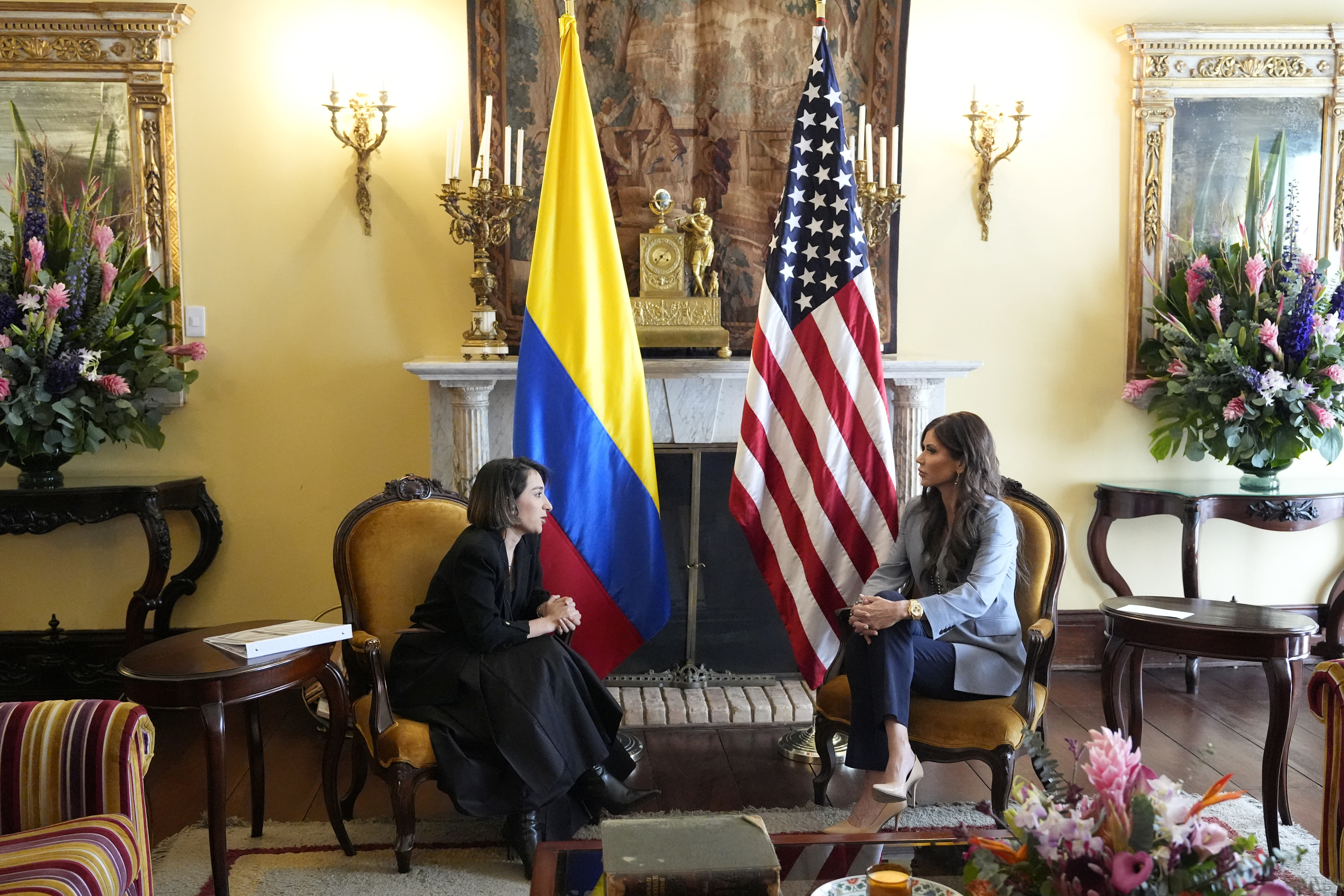 Kristi Noem and Laura Sarabia sit next to US and Colombian flags.