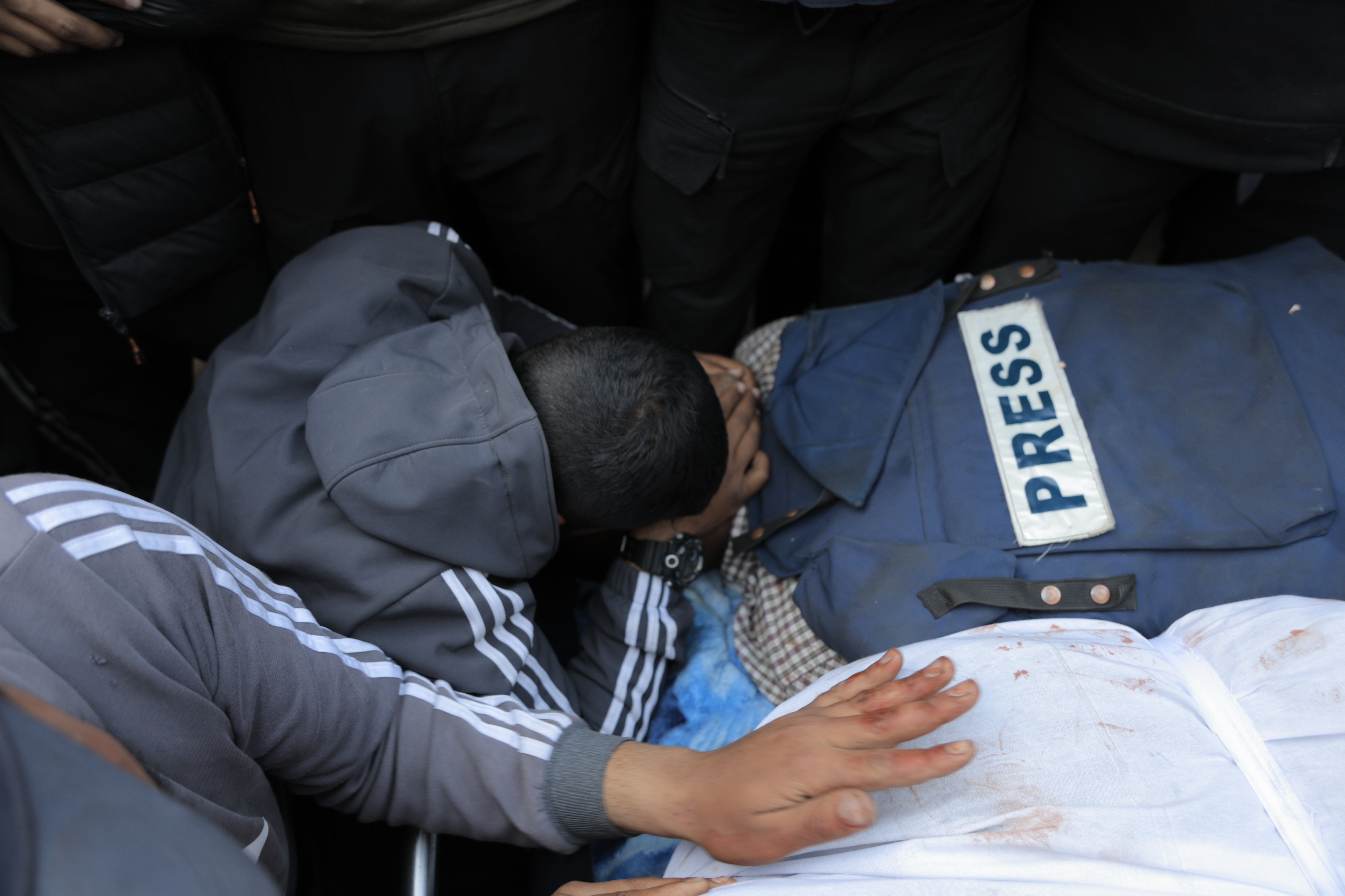 Hossam Shabat's shrouded boyd, with his press vest on top of it, is bid farewell by his family, friends and colelagues