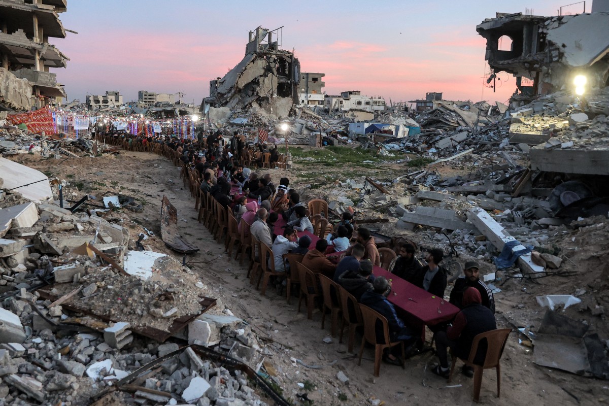 People gather by the rubble of destroyed buildings for a mass gathering for a communal iftar fast-breaking meal on the second day of the Muslim holy month of Ramadan in the area of al-Dahduh in Gaza City's Tal al-Hawa district on March 2, 2025 amid the ongoing truce in the war between Israel and Hamas. (Photo by Omar AL-QATTAA / AFP)