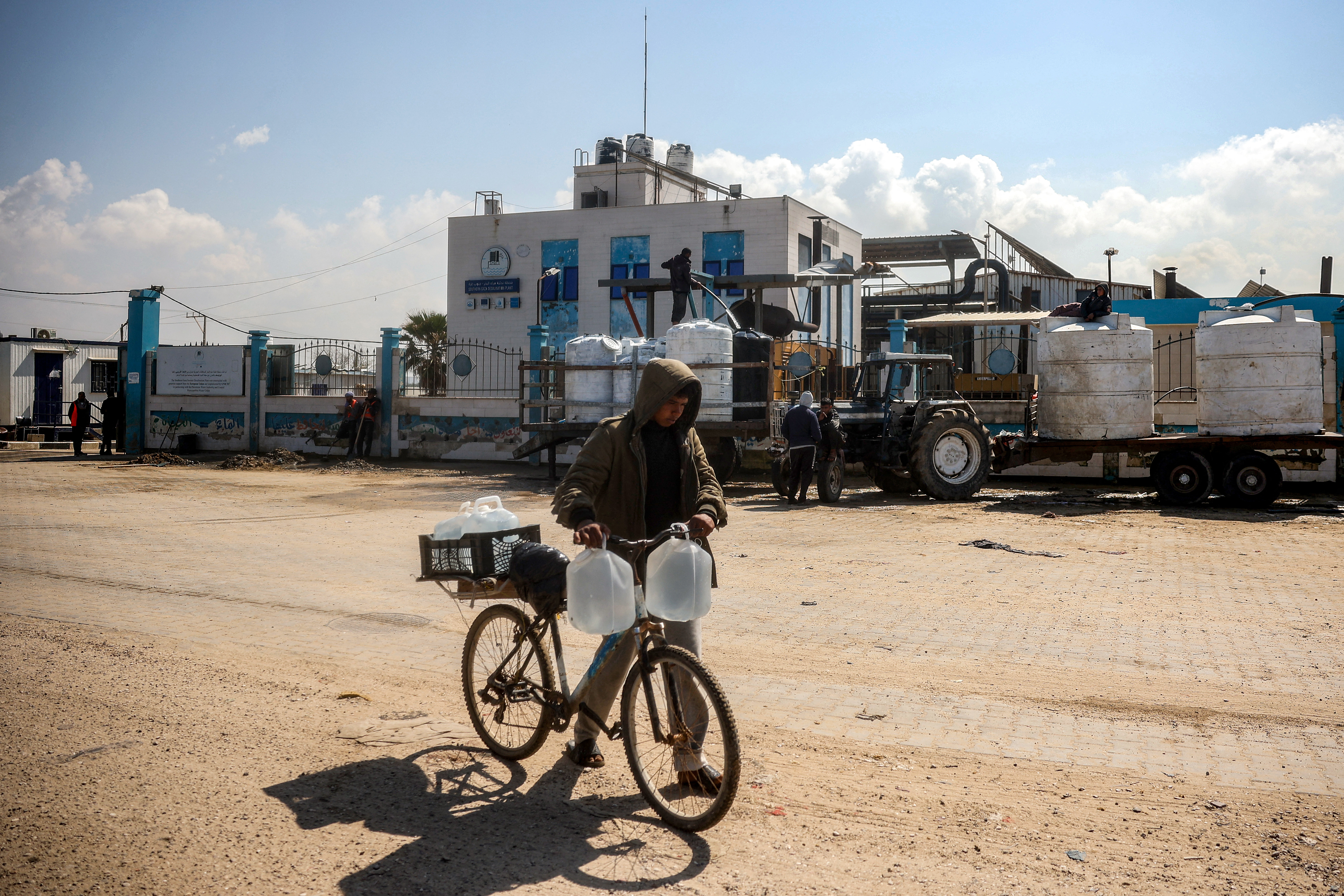 A youth pushes a bicycle loaded with filled-up water containers outside the Southern Gaza Desalination plant, which stopped working after Israel cut off electricity supply to the Gaza Strip, in Deir el-Balah in the centre of the Palestinian territory on March 10, 2025. Israel is due to send a delegation to Doha on March 10 for a fresh round of talks on extending a fragile ceasefire in Gaza, after cutting off electricity to ramp up pressure on Hamas. The first phase of the truce ended on March 1 with no agreement on subsequent stages that could secure a permanent end to the war, but both sides have since refrained from resuming full-scale fighting. (Photo by Eyad BABA / AFP)