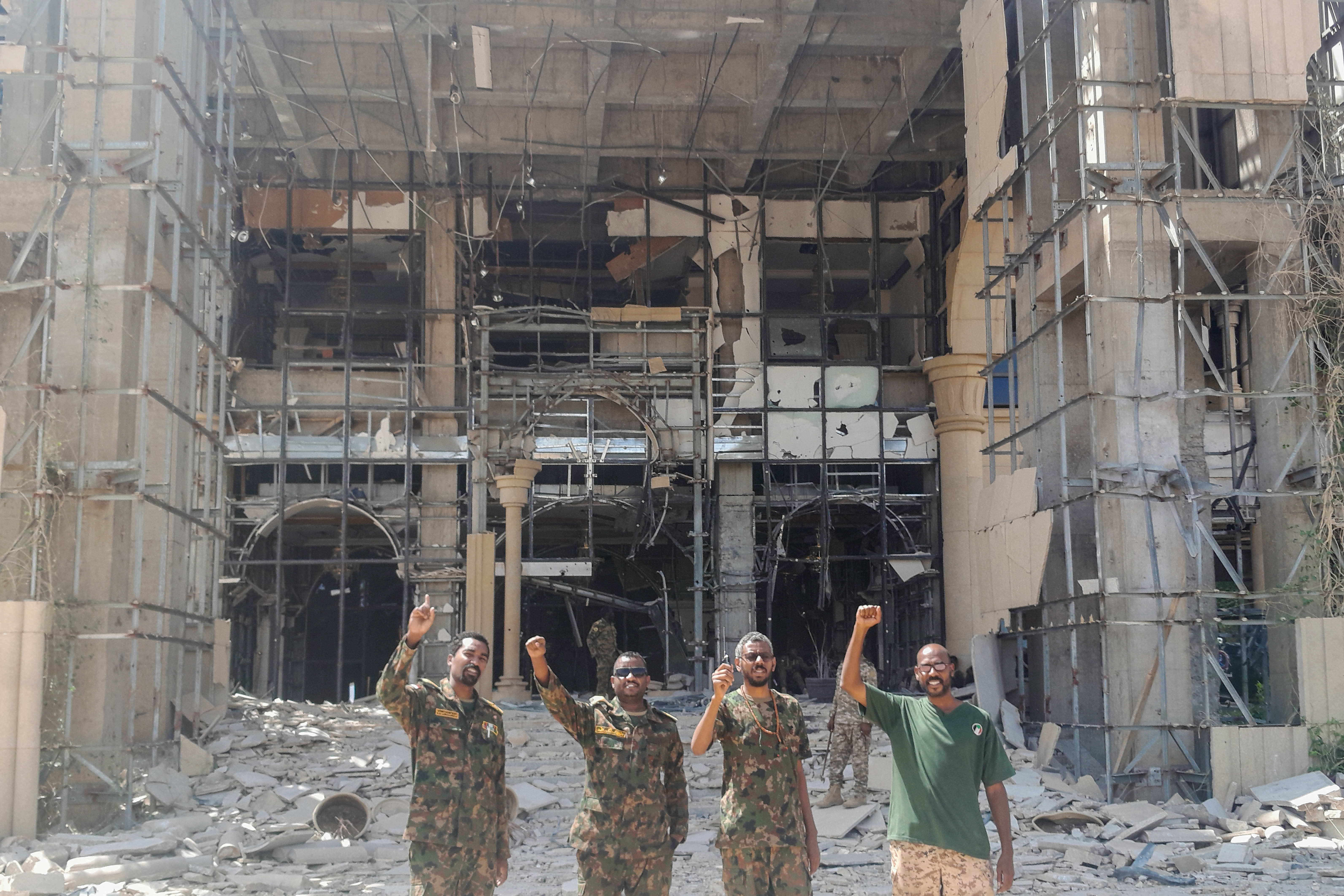 Soldiers of the Sudanese army or affiliated forces pose for a picture while pumping their fists in front of the damaged presidential palace.