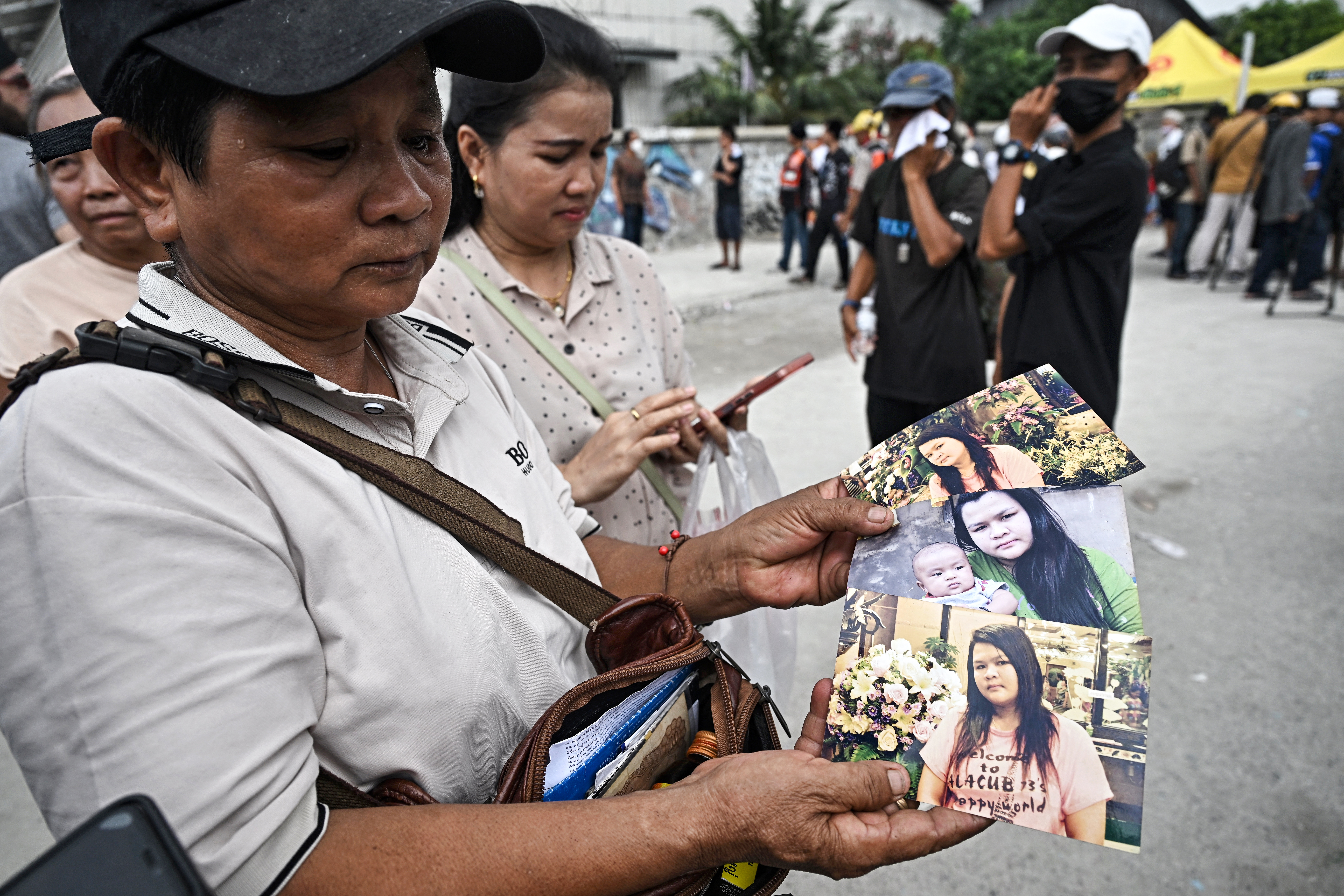 Wassana Phromma (L), from Thailand's northeastern province of Khon Kaen, shows photographs of her missing daughter Anusara, 35, at the site of an under-construction building collapse in Bangkok on March 30, 2025, two days after an earthquake struck central Myanmar and Thailand.